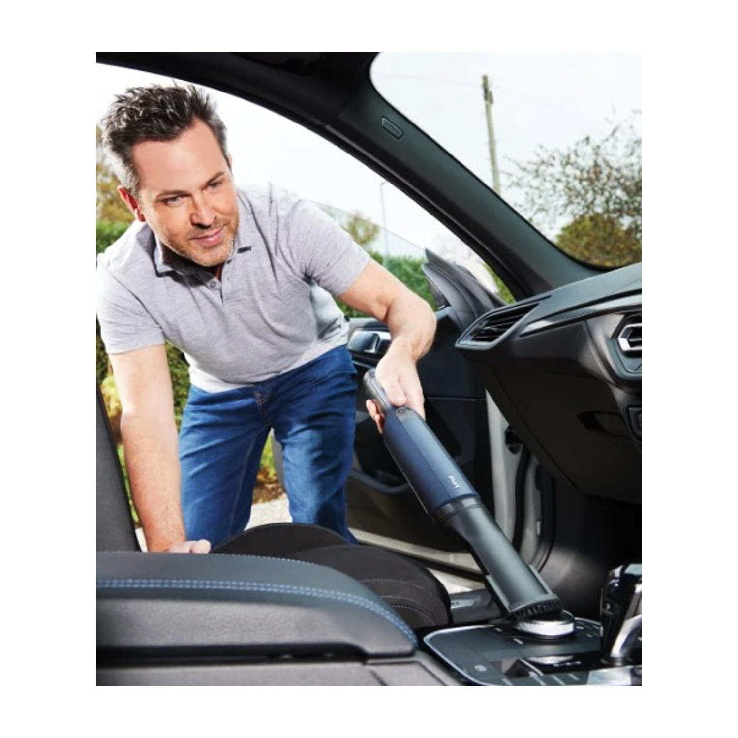 L'uomo aspira l'interno dell'auto. Tiene in mano un aspirapolvere nero e blu.