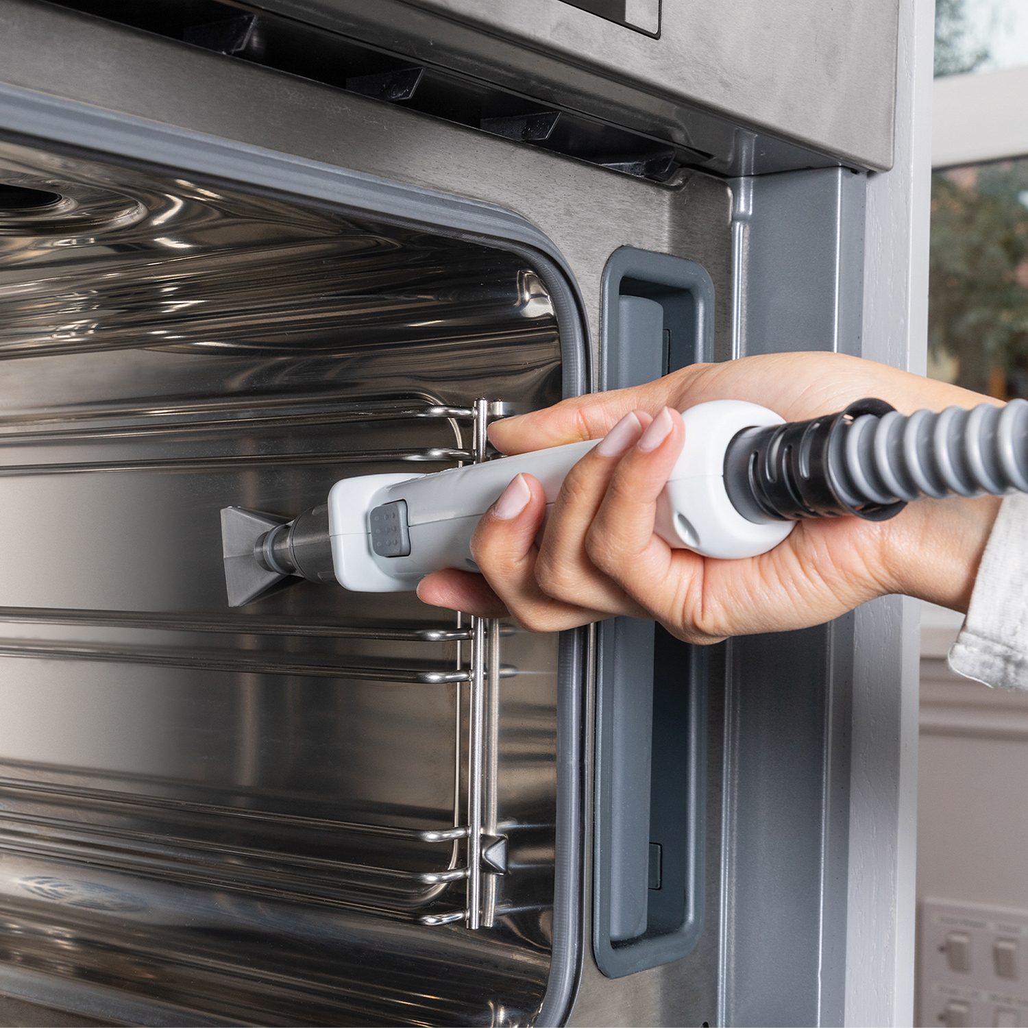 La mano di una persona che tiene uno strumento di pulizia all'interno di un forno in acciaio inossidabile.