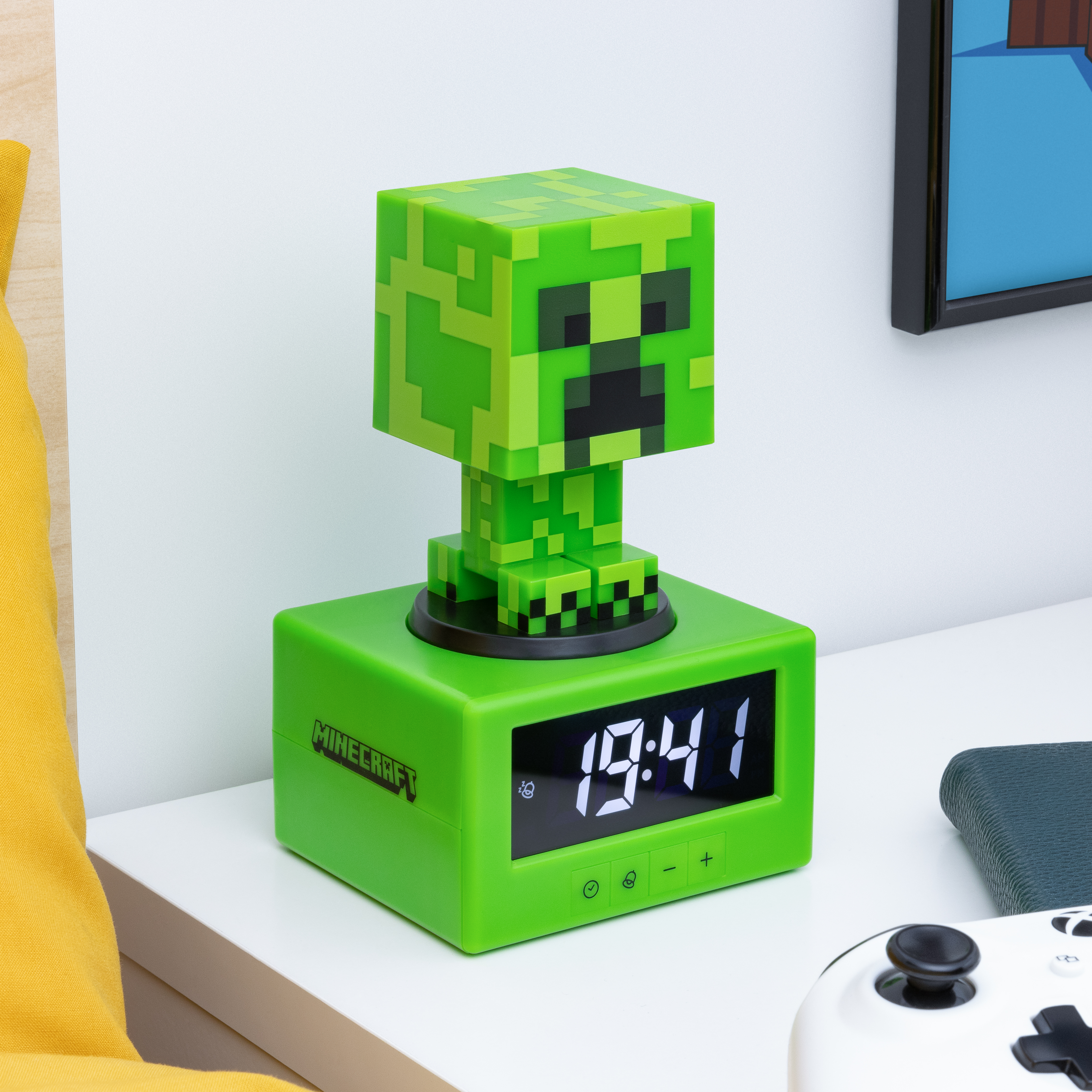 Grüner Minecraft Creeper Wecker auf weißem Tisch. Zeigt 19:41 an. Controller und gelbes Kissen in der Nähe.