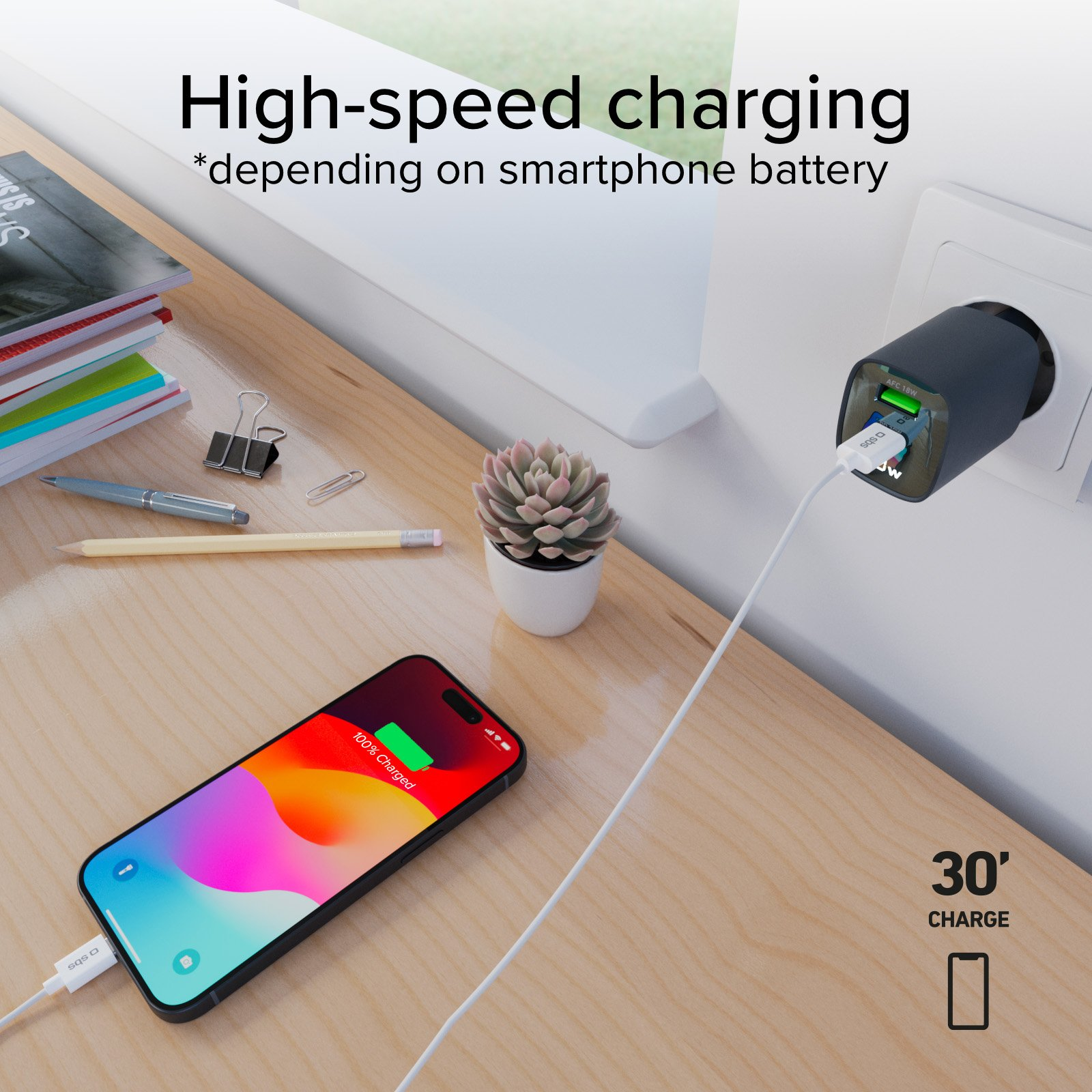 Telefon ładujący się na biurku, z ładowarką podłączoną do ściany. Telefon pokazuje 100% naładowania.