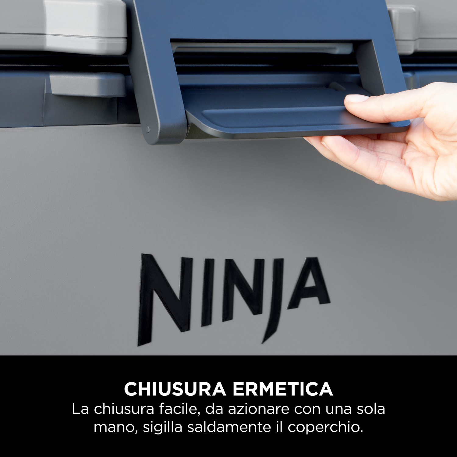 Mano che apre il coperchio nero del frigorifero. Logo Ninja sul frigorifero. Superficie grigia.