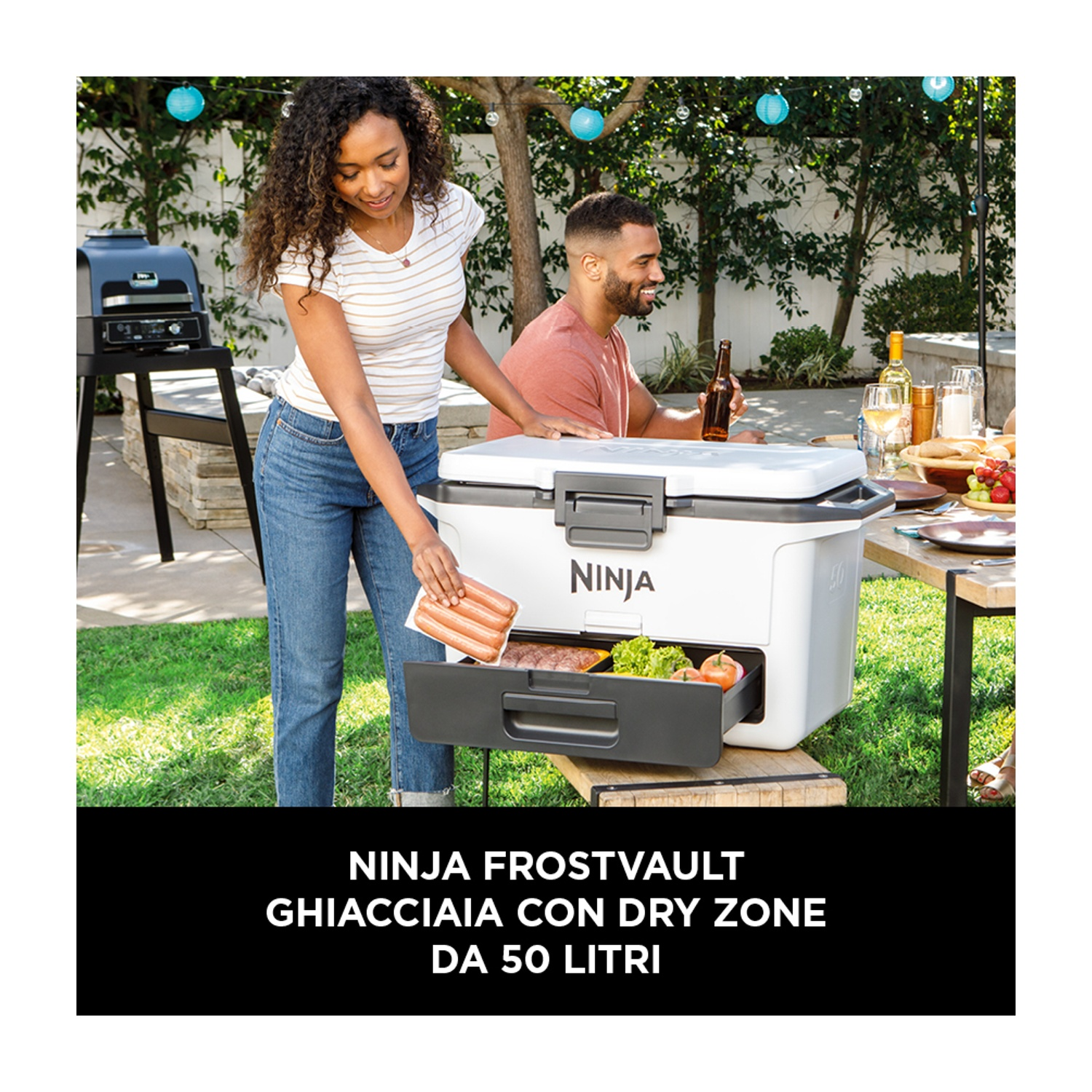 Una donna consegna hot dog a un uomo a un picnic. Una ghiacciaia bianca è tra loro.