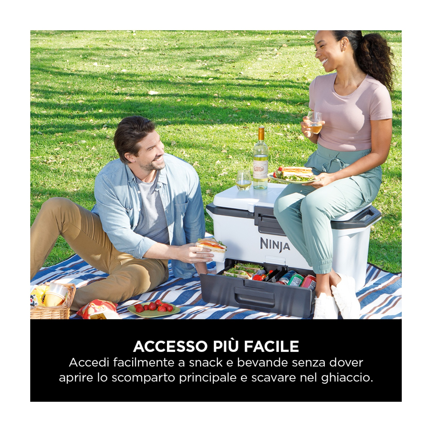 Una coppia è su una coperta da picnic, beve vino e mangia panini. Ghiacciaia nelle vicinanze.