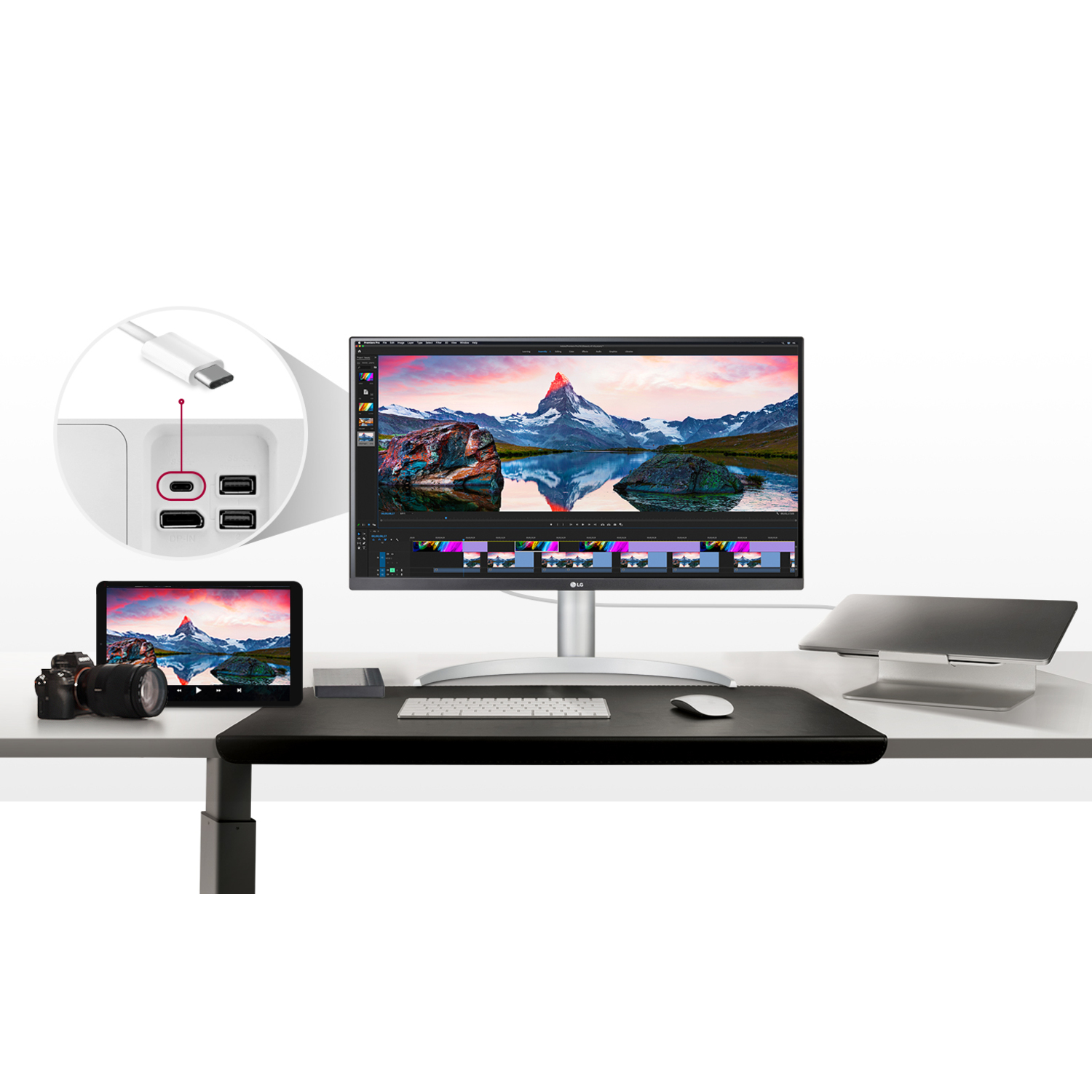 Desktop setup with a monitor, camera, tablet, keyboard, and laptop on a white desk.