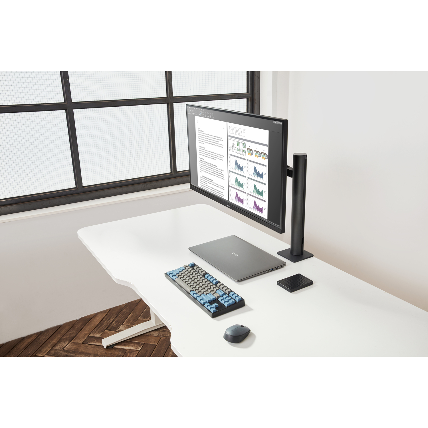 Bureau blanc avec un ordinateur portable, un moniteur, un clavier, une souris et des accessoires noirs près d'une fenêtre.