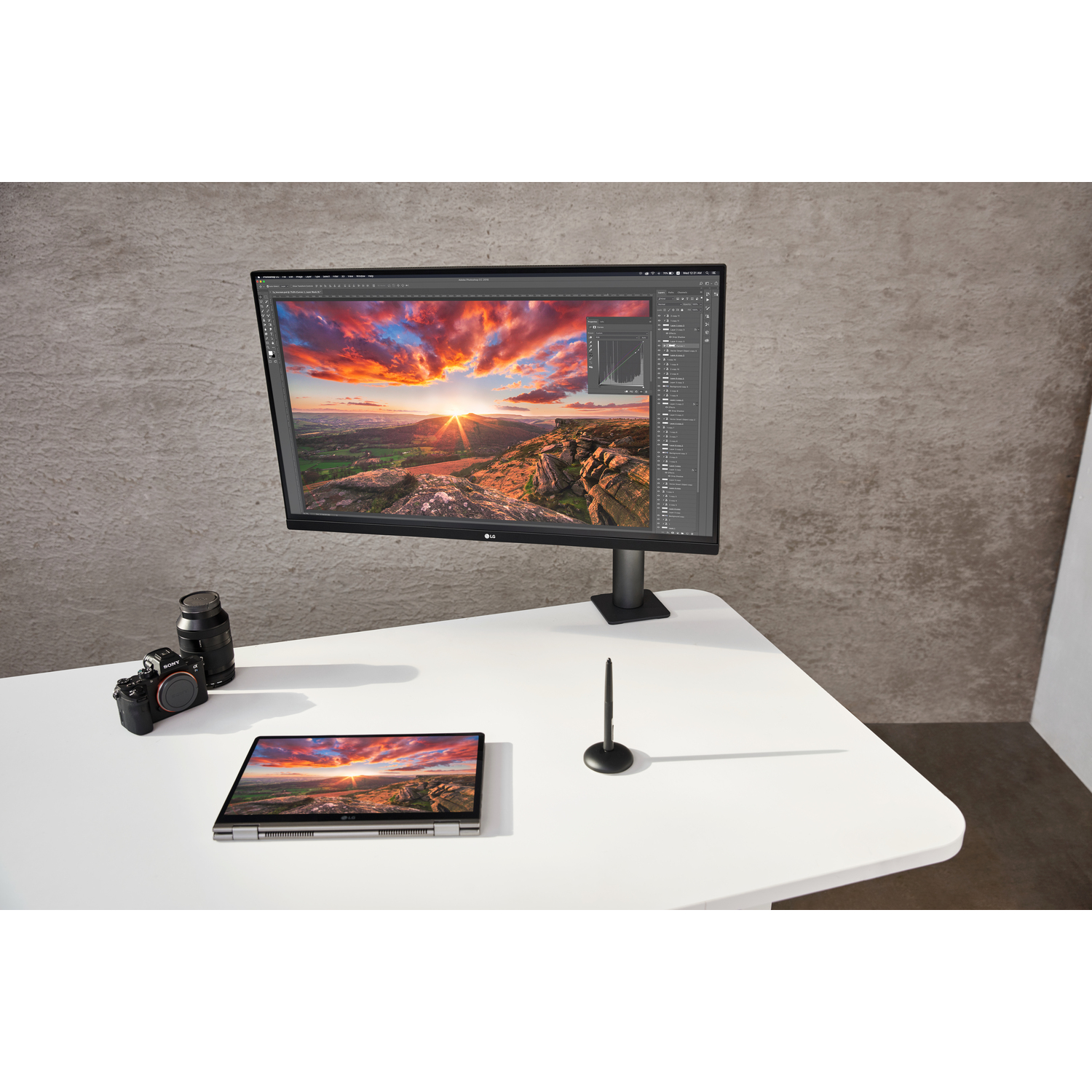 Un moniteur sur pied, un ordinateur portable, un stylo et un appareil photo sur un bureau blanc.