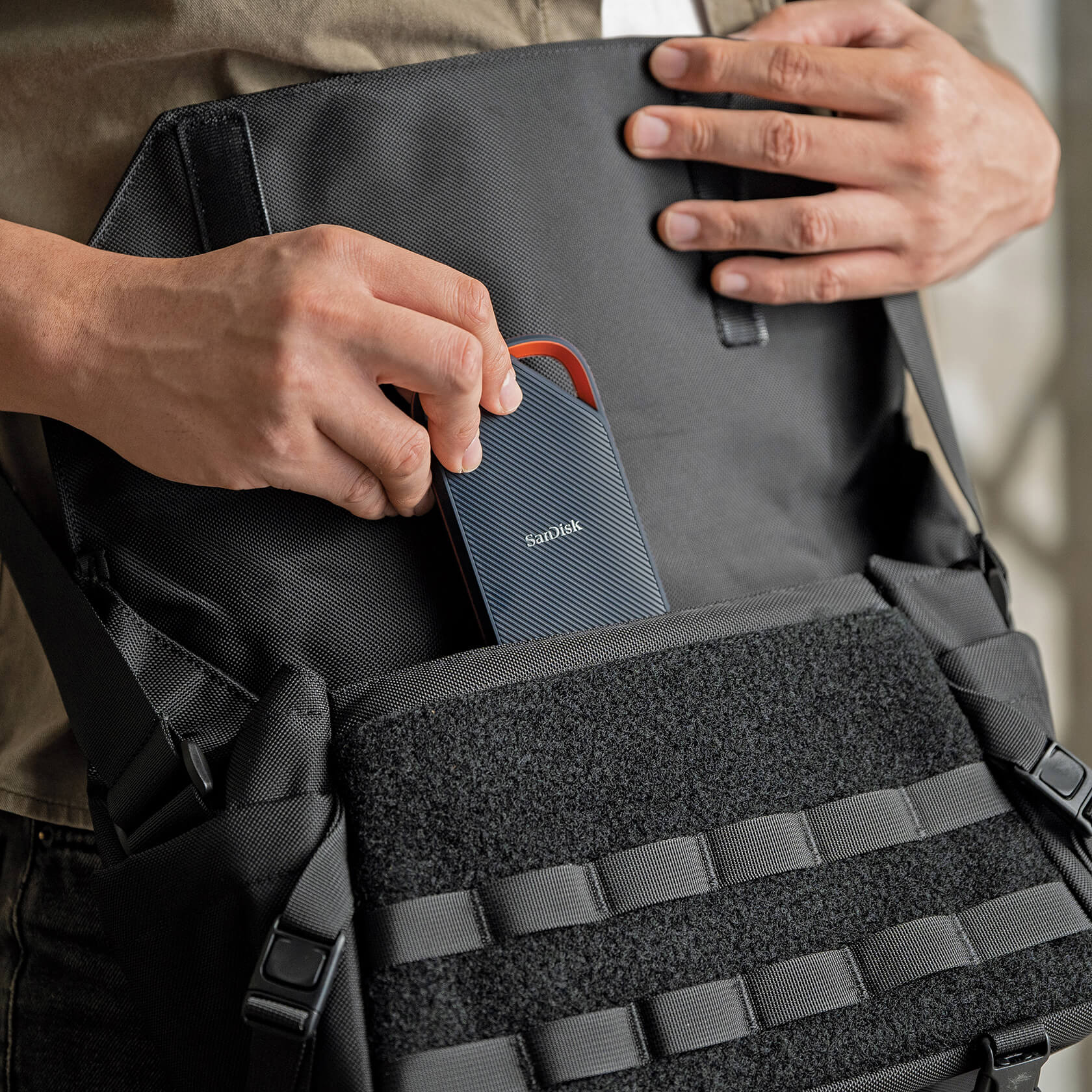 Eine Person legt eine dunkelblaue tragbare Festplatte von SanDisk in eine schwarze Messenger-Tasche.