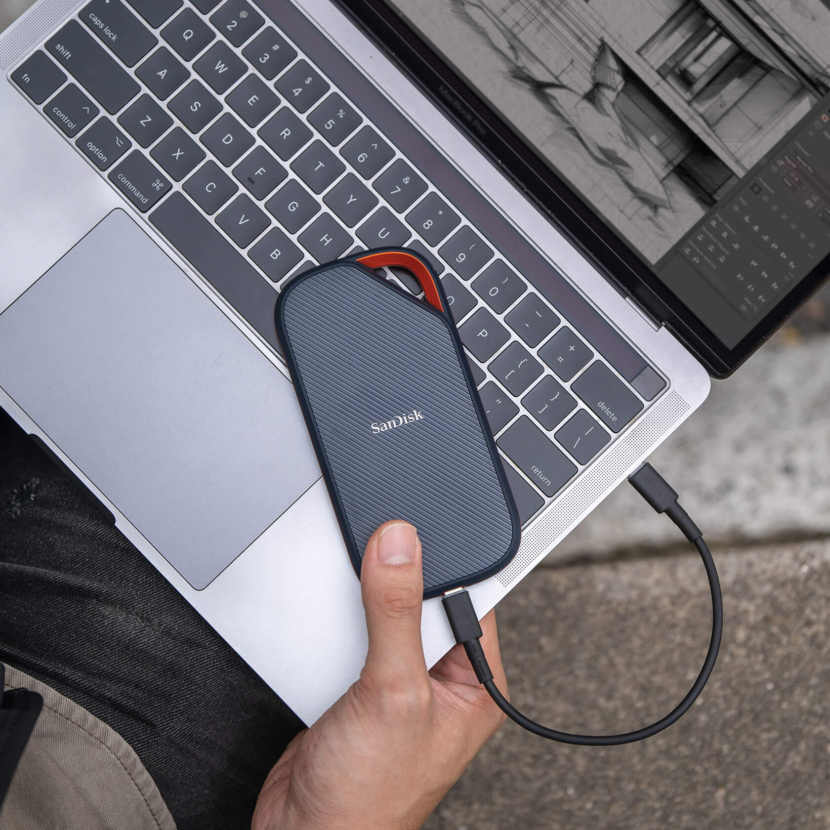 Sandisk tragbare Festplatte an einem Laptop angeschlossen. Hand hält das Laufwerk. Grauer Laptop.