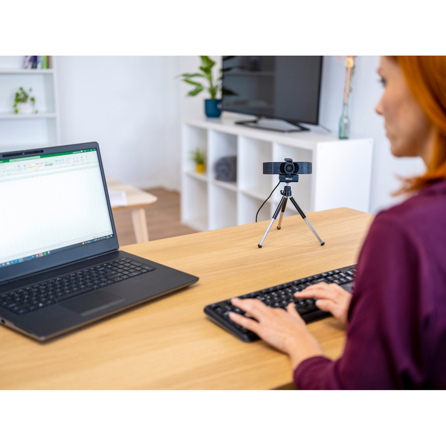 Donna che usa un laptop e una tastiera con una webcam su una scrivania.