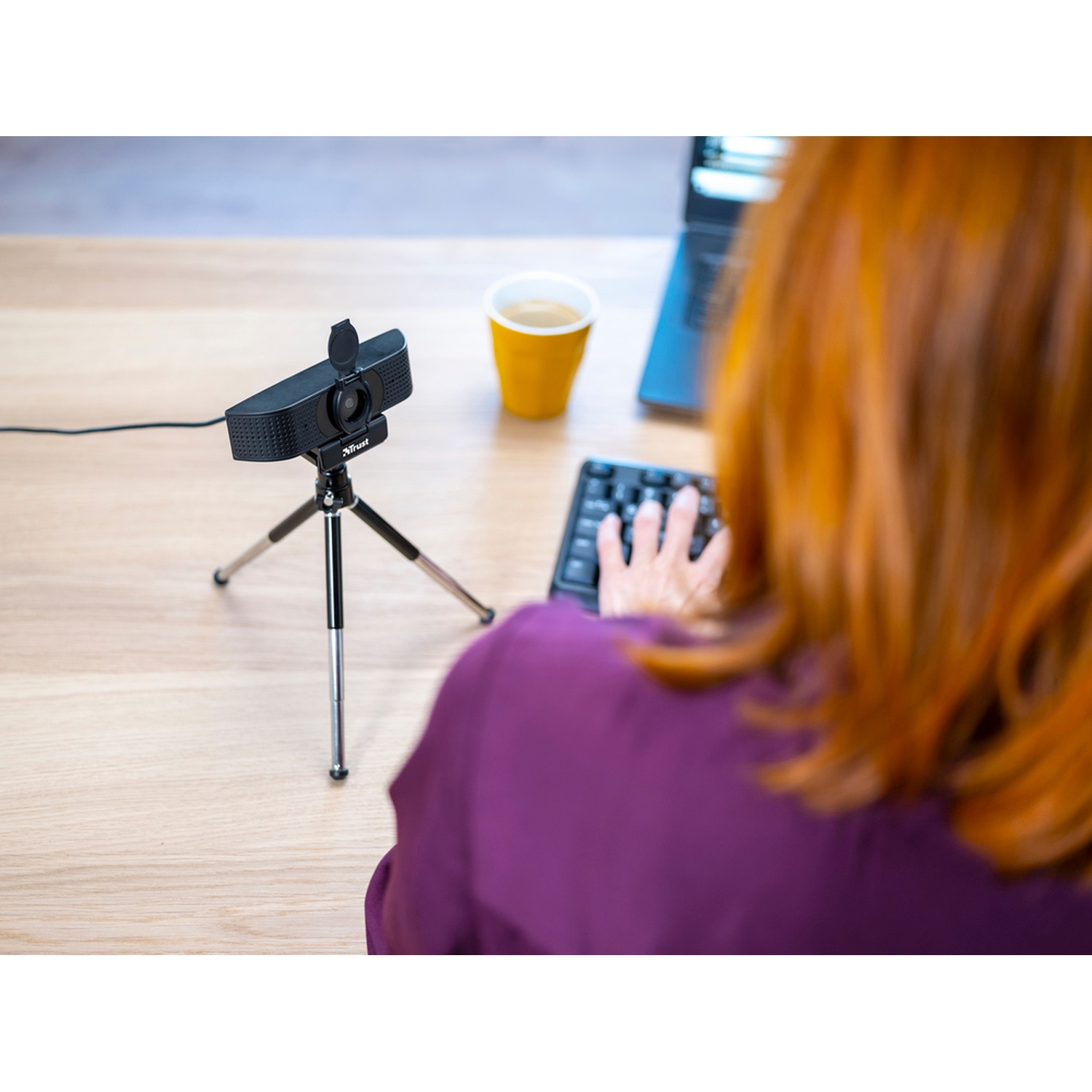Una persona usa una tastiera nera con una webcam su un treppiede. Una tazza di caffè è accanto.