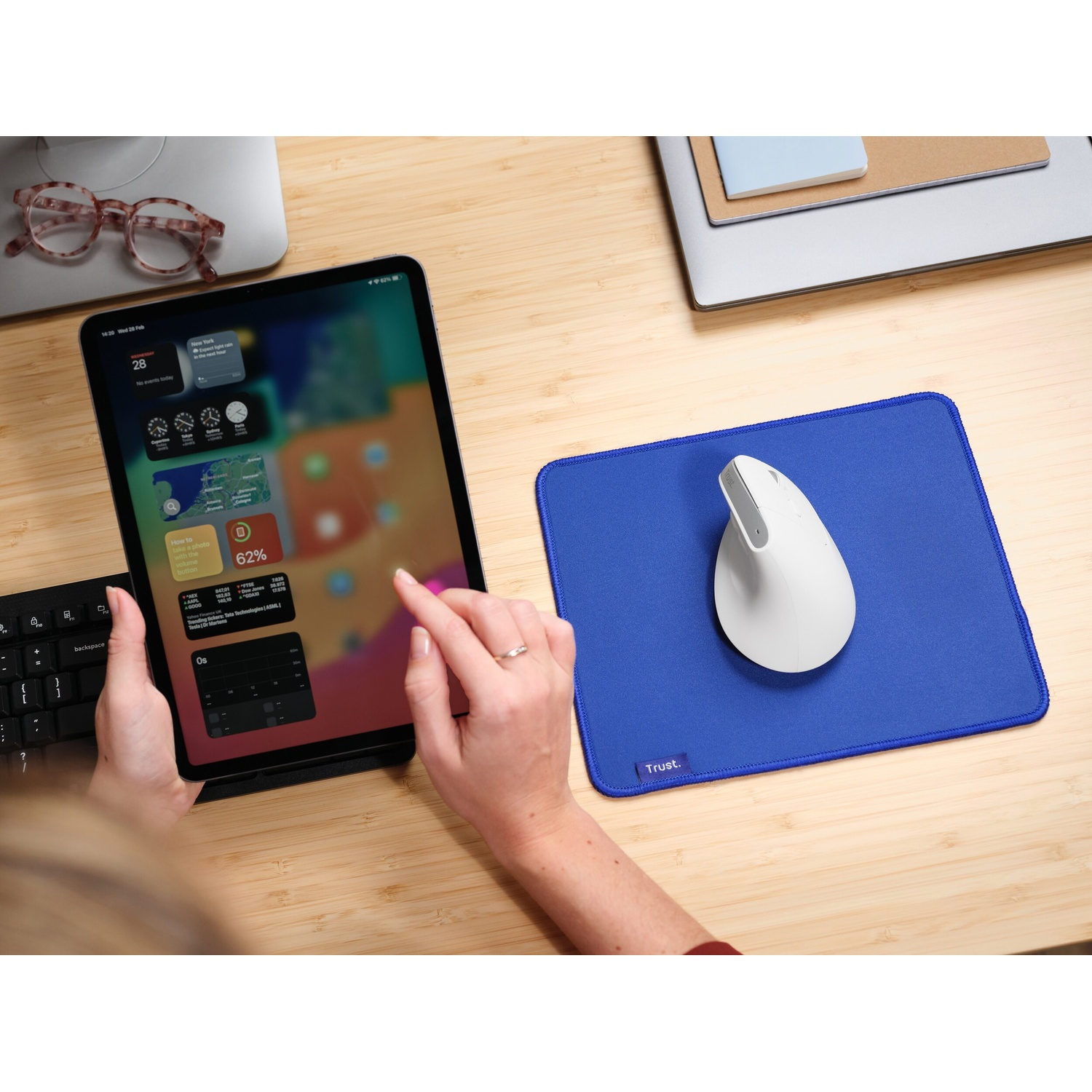Un mouse bianco su un tappetino blu accanto a un tablet con tastiera e occhiali.