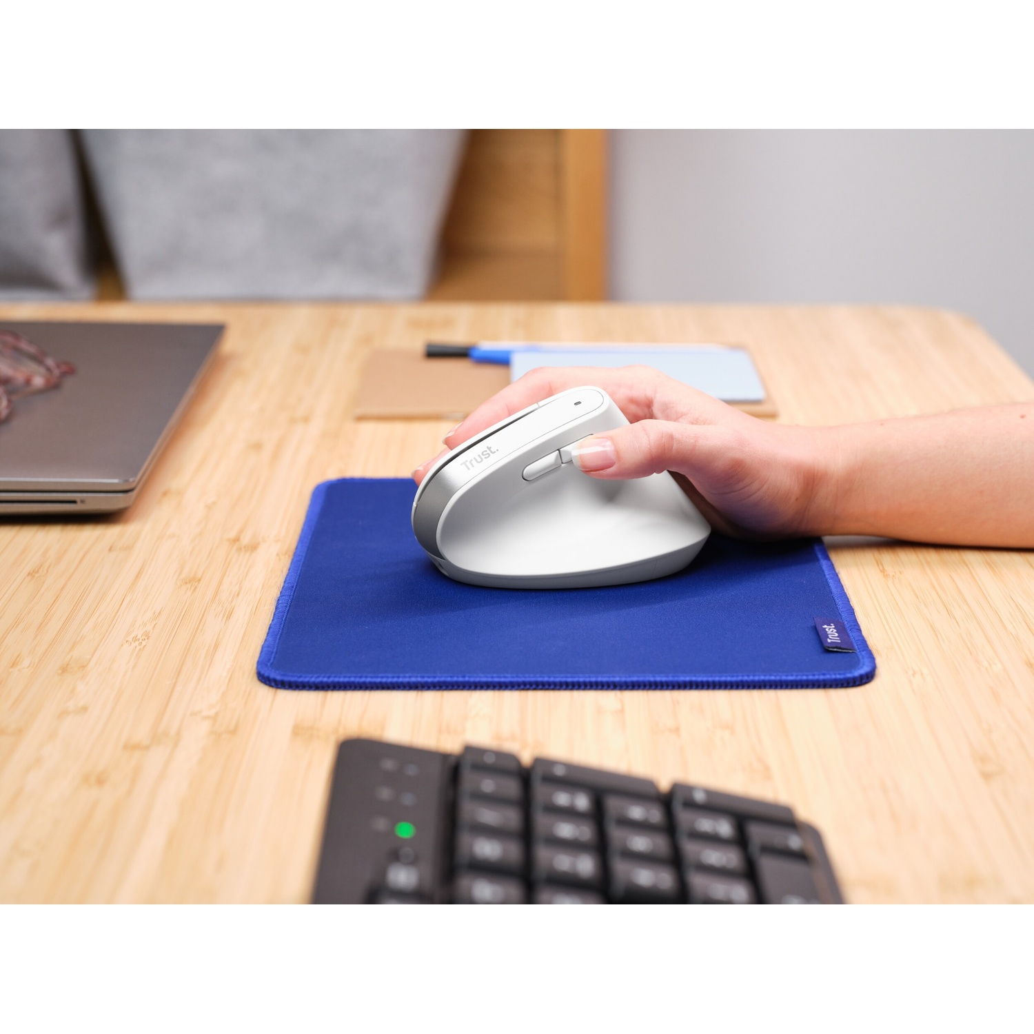Una persona usa un mouse ergonomico bianco su un tappetino blu su una scrivania.