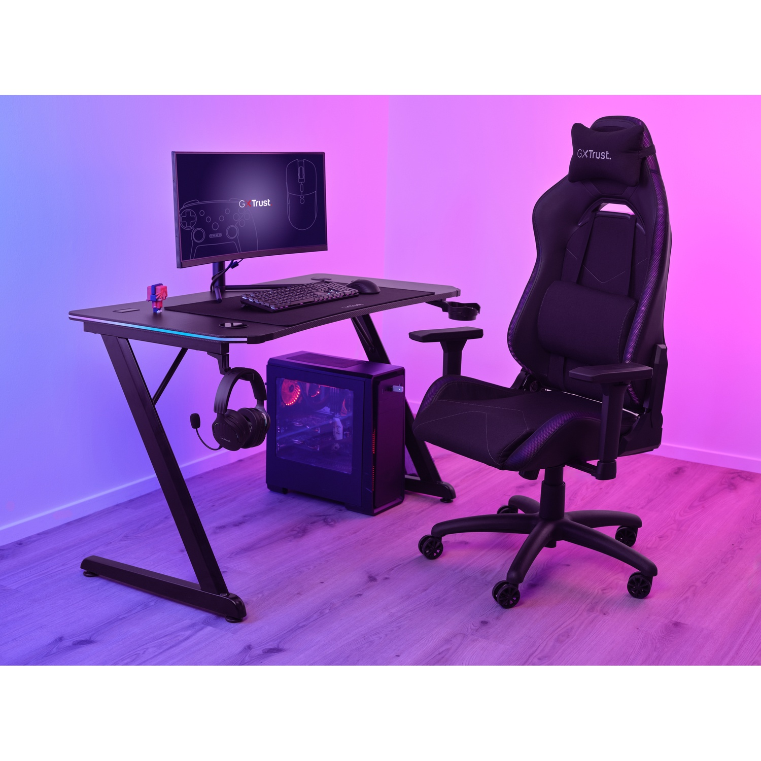 Configurazione di gioco: scrivania nera, monitor, PC, cuffie e sedia. Illuminazione viola e blu sulla parete.