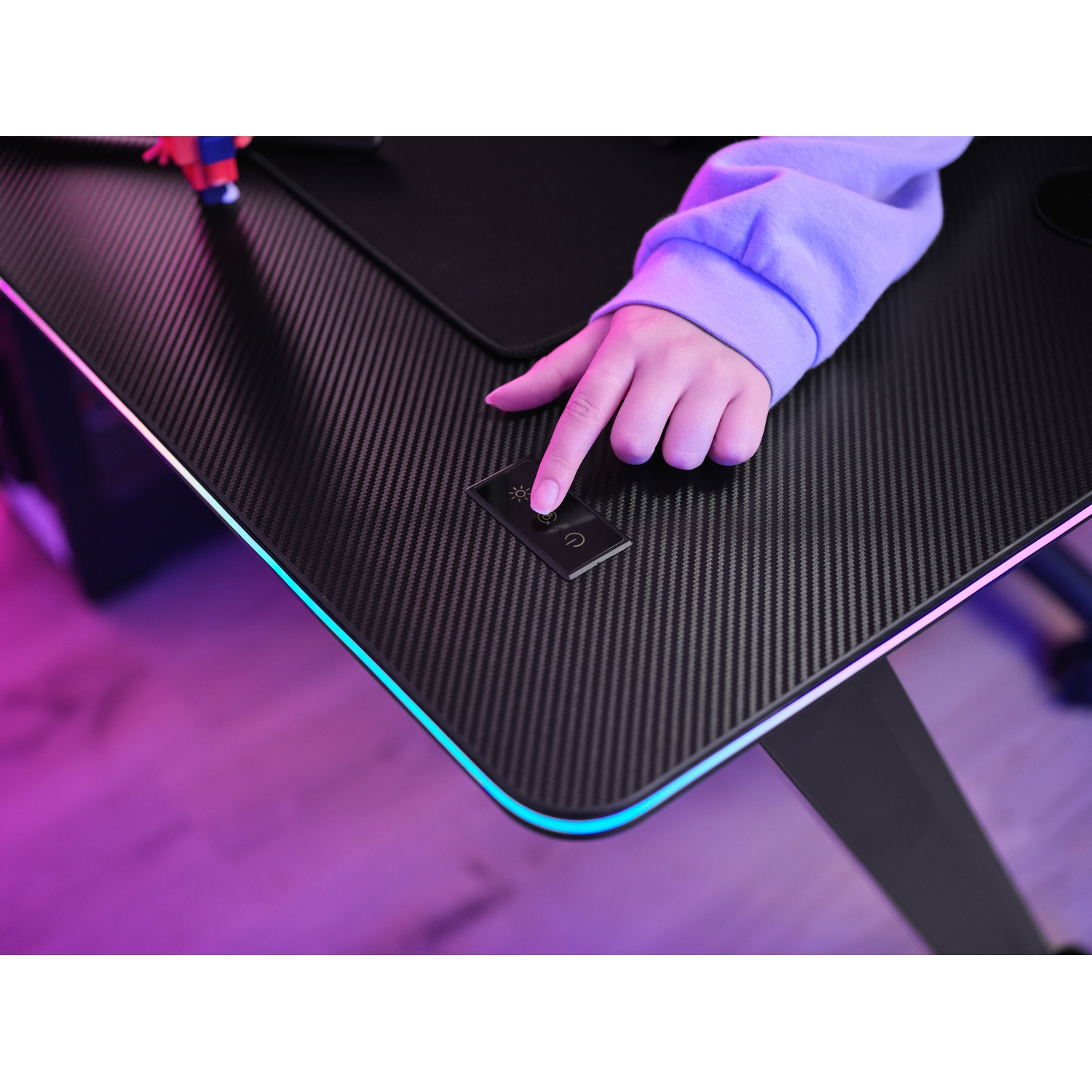 Mano che preme un pulsante su una scrivania nera con texture in fibra di carbonio, illuminazione LED sul bordo.