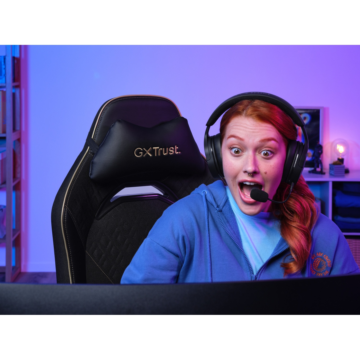 Una donna con i capelli rossi che indossa un auricolare, sorpresa, seduta su una sedia da gioco. La scena ha un bagliore blu e viola.