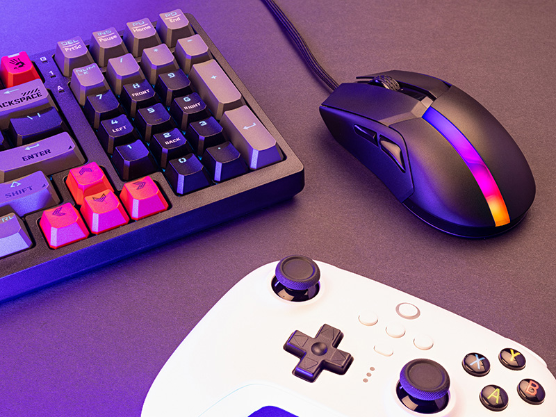 Konfiguracja do gier z klawiaturą, myszą i kontrolerem na ciemnej powierzchni z fioletowym oświetleniem.