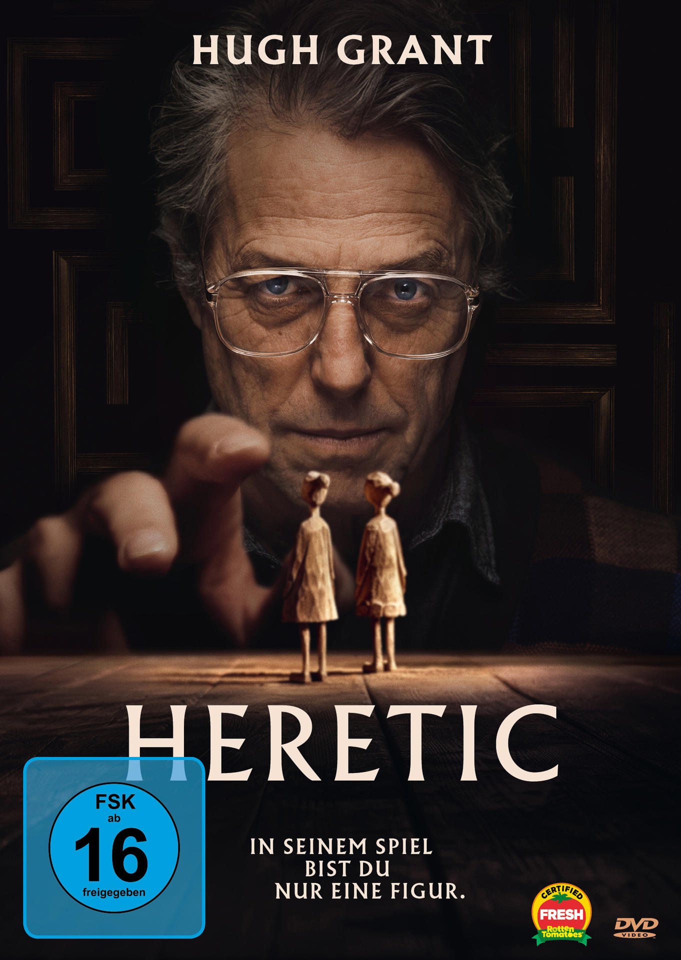 Filmcover: Hugh Grants Gesicht blickt auf zwei Holzfiguren. Titel: Ketzer.