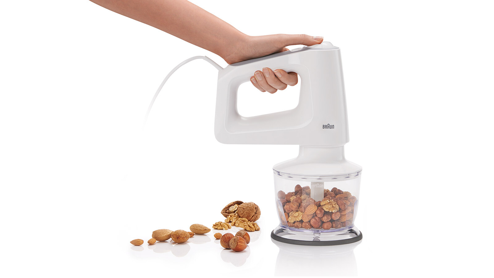 Eine Hand, die einen weißen Braun-Zerkleinerer mit Nüssen hält.