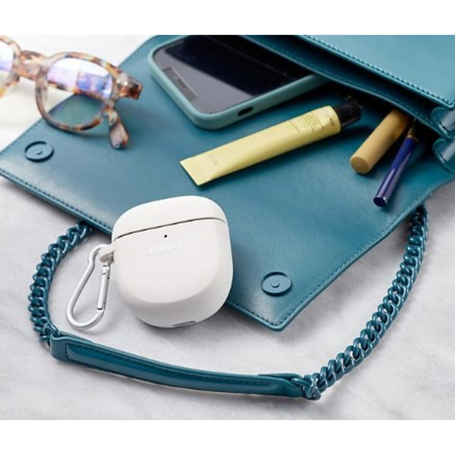 Custodia per auricolari bianca, occhiali, telefono e altri oggetti in una borsa verde acqua.