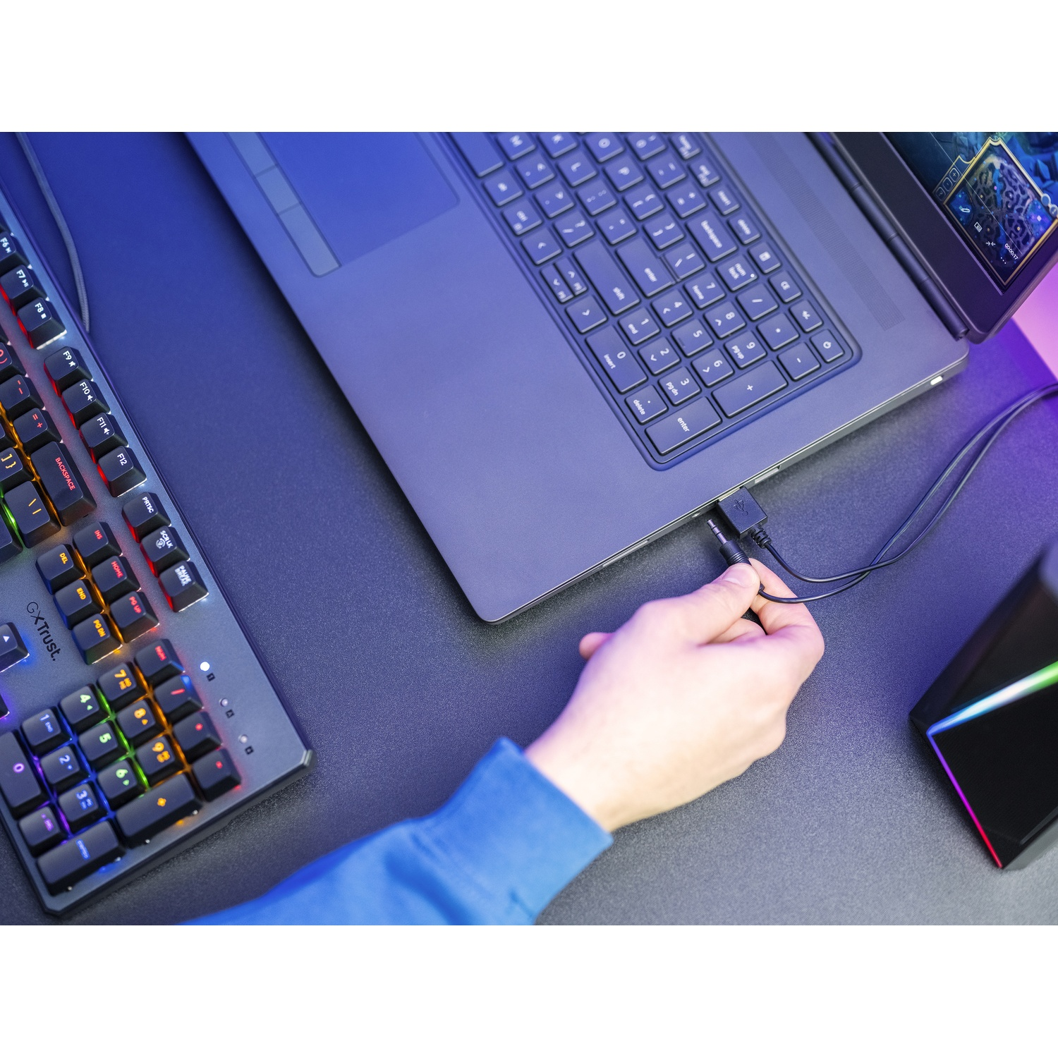 Un laptop collegato a una tastiera e a un dispositivo nero, con la mano di una persona che collega un cavo.