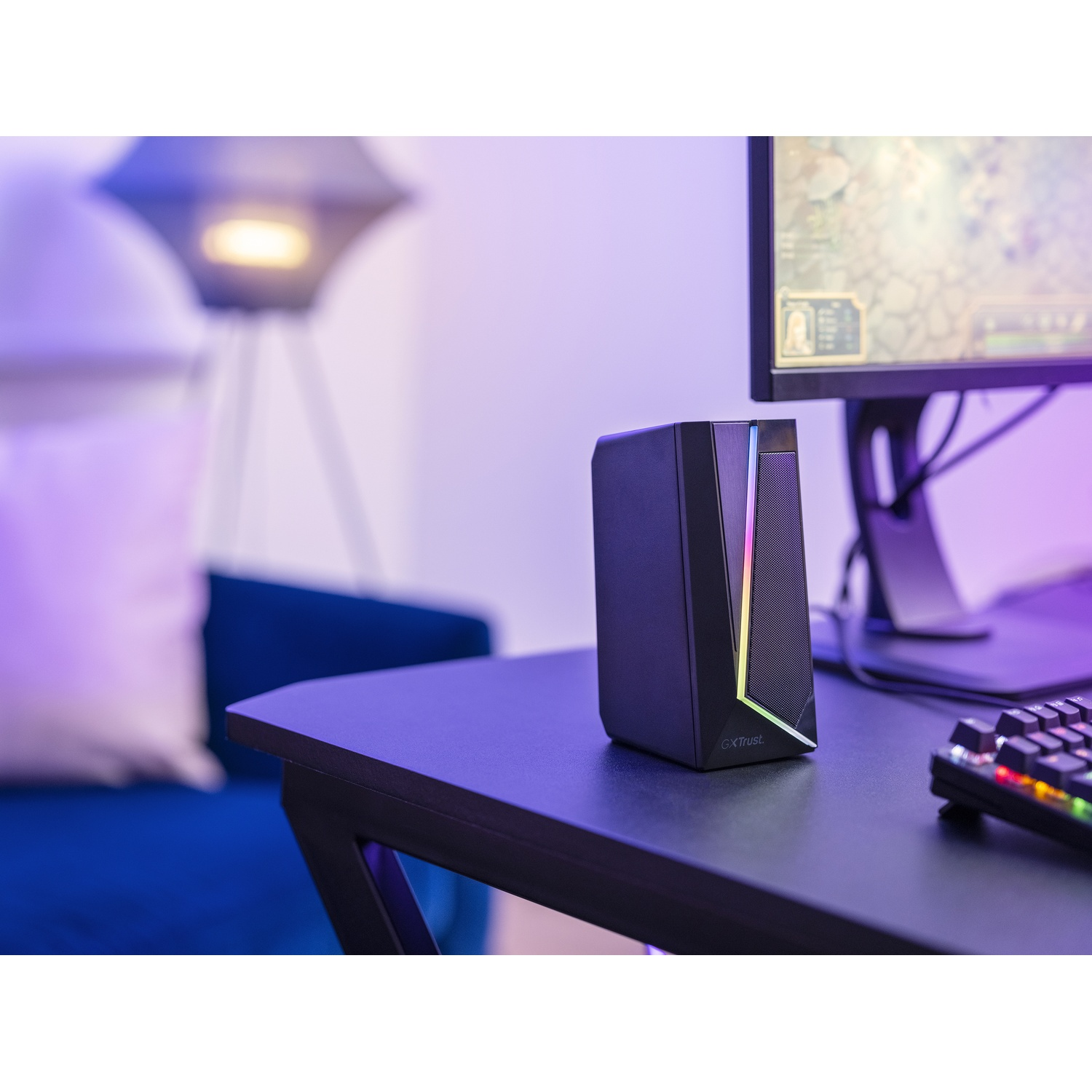 Altoparlante nero su scrivania, monitor sullo sfondo, illuminazione blu e viola.