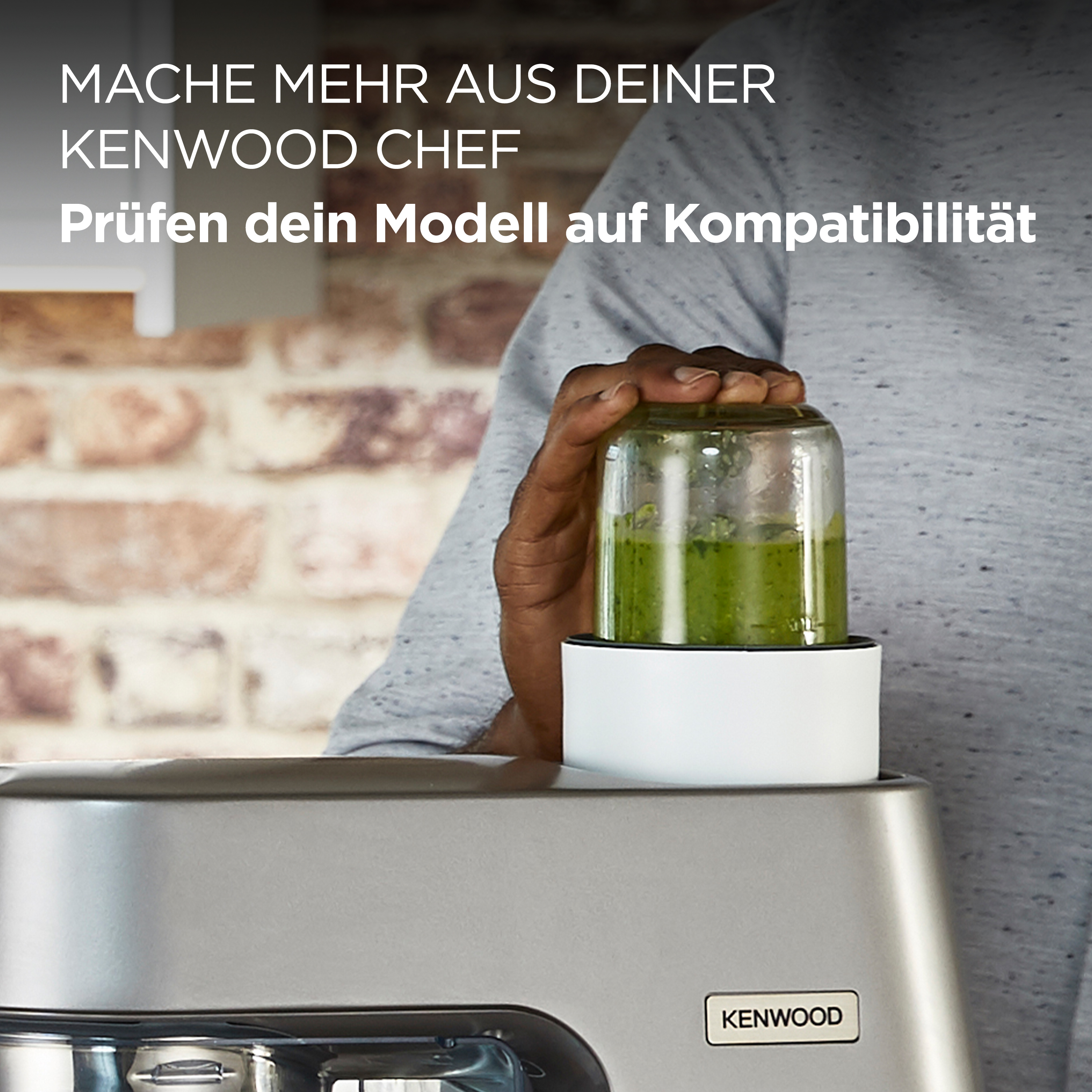 Eine Person, die einen Mixerbehälter mit grüner Substanz über einer Kenwood Chef Küchenmaschine hält.