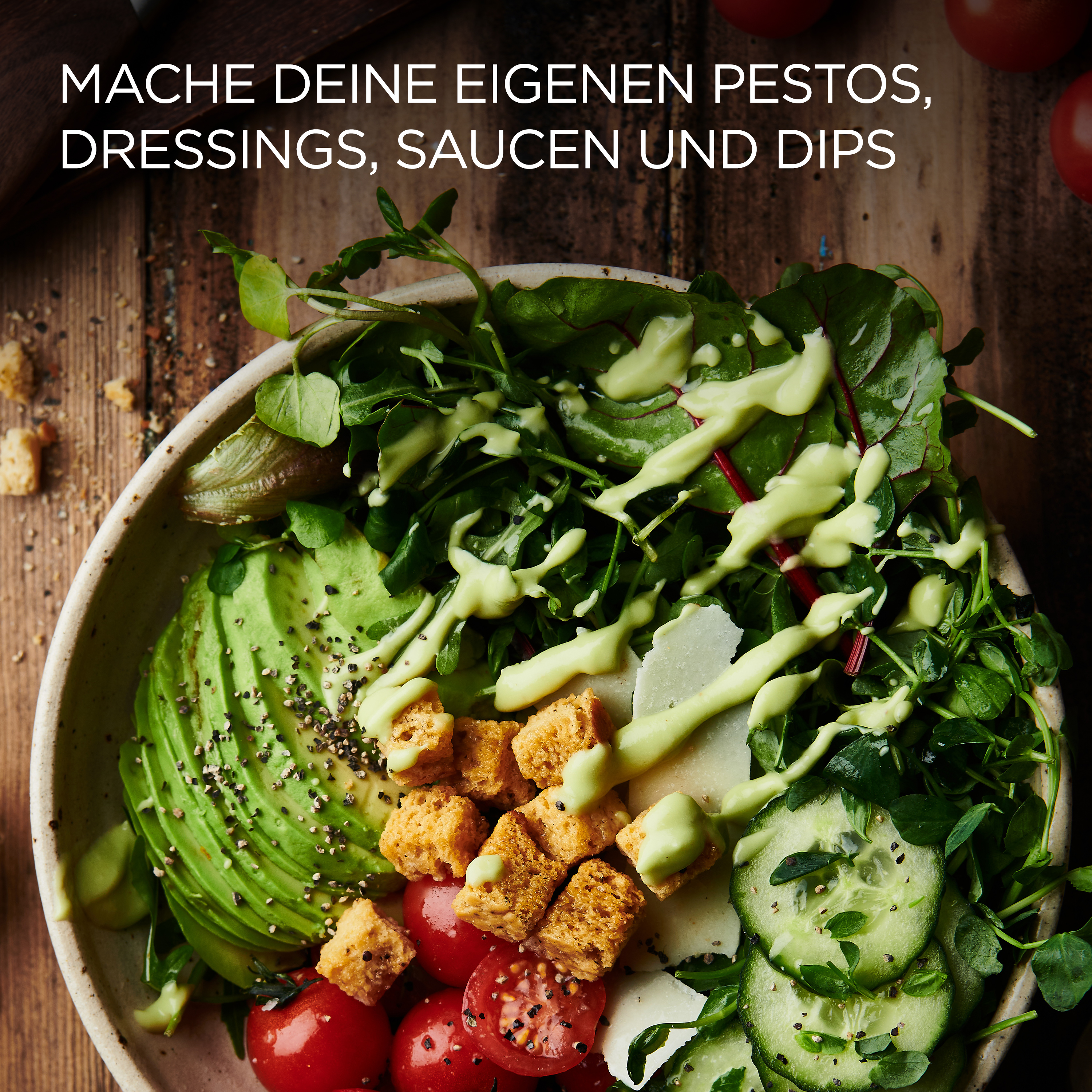 Eine Schüssel Salat mit Avocado, Tomaten und Croutons. Grünes Dressing ist darüber geträufelt. Holzoberfläche.