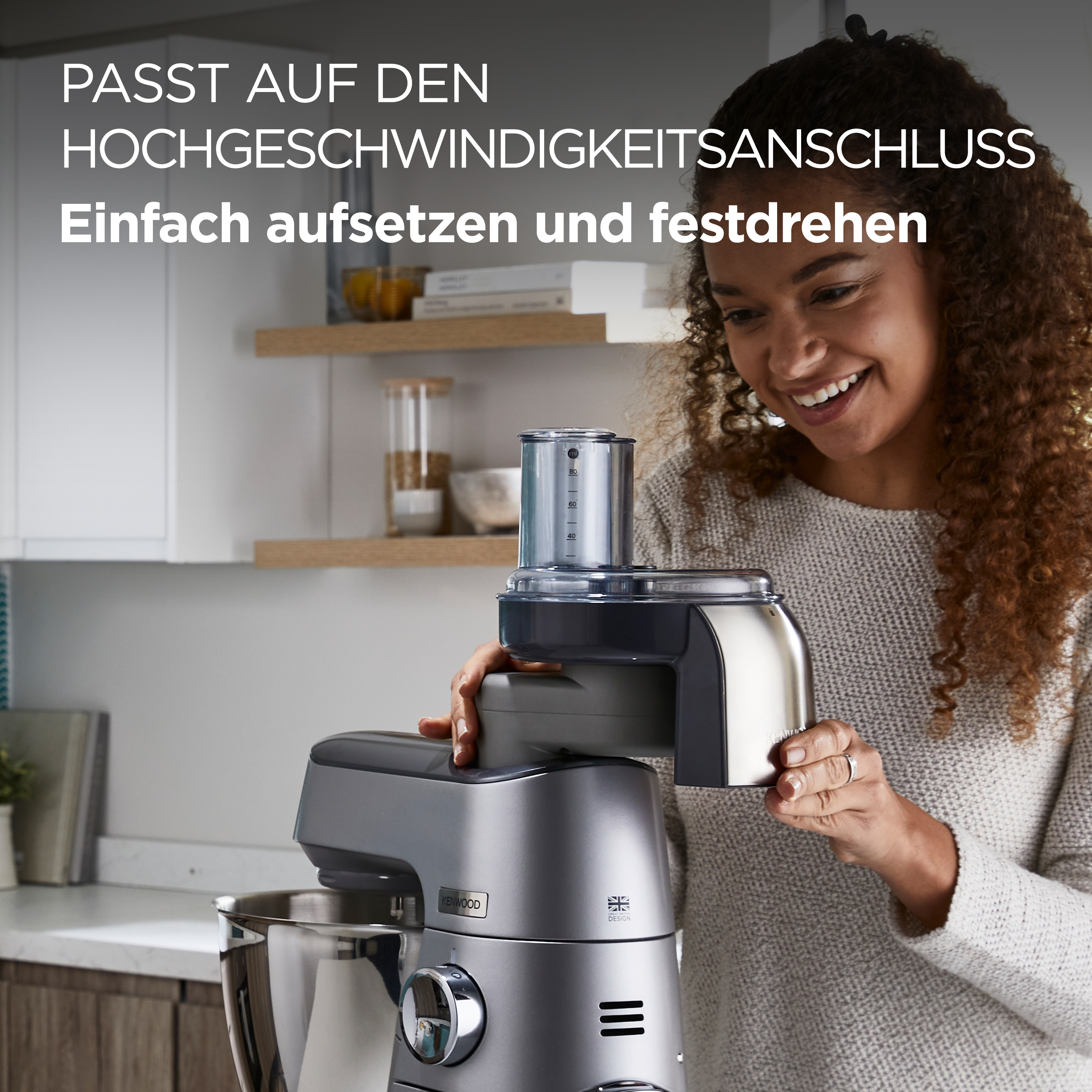 Eine Frau befestigt ein Teil des Küchengeräts an einem Kenwood-Mixer. Sie lächelt.