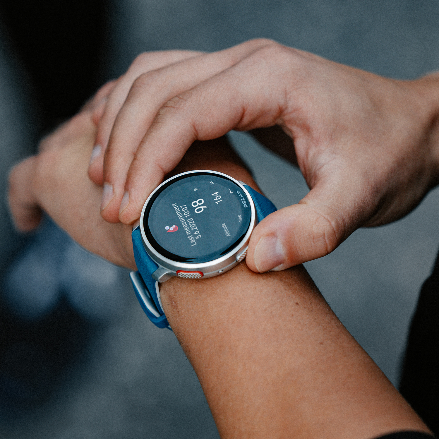 Persona con un reloj inteligente con banda azul en la muñeca, mostrando la frecuencia cardíaca y la hora.