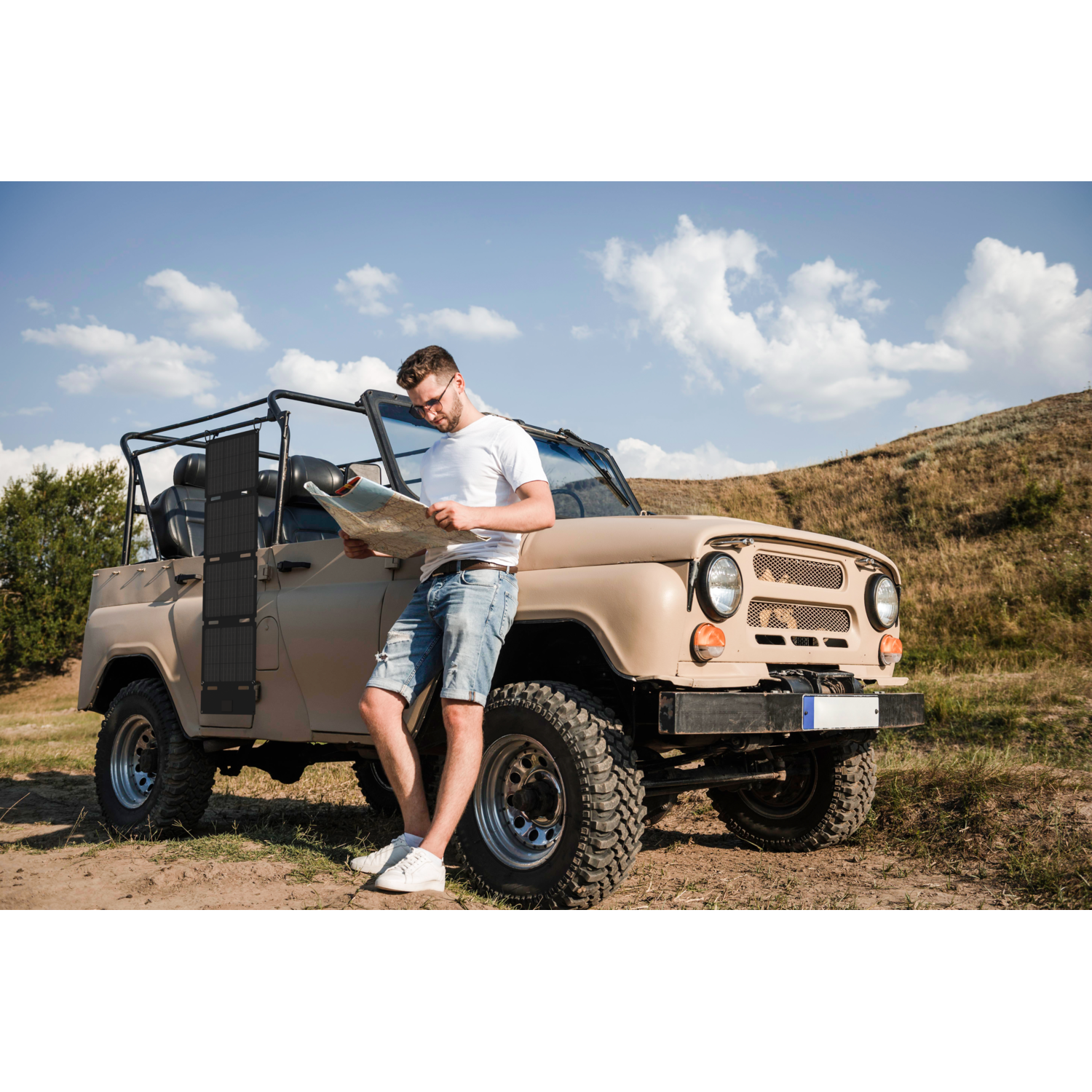 Man in een veld bekijkt een kaart, leunend op een beige jeep met een zonnepaneel.