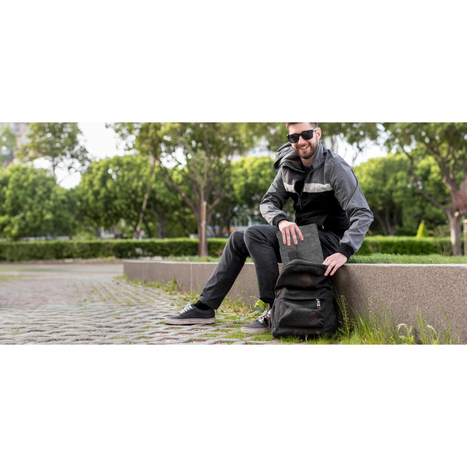 Man zit en stopt een tablet in een rugzak in een park.