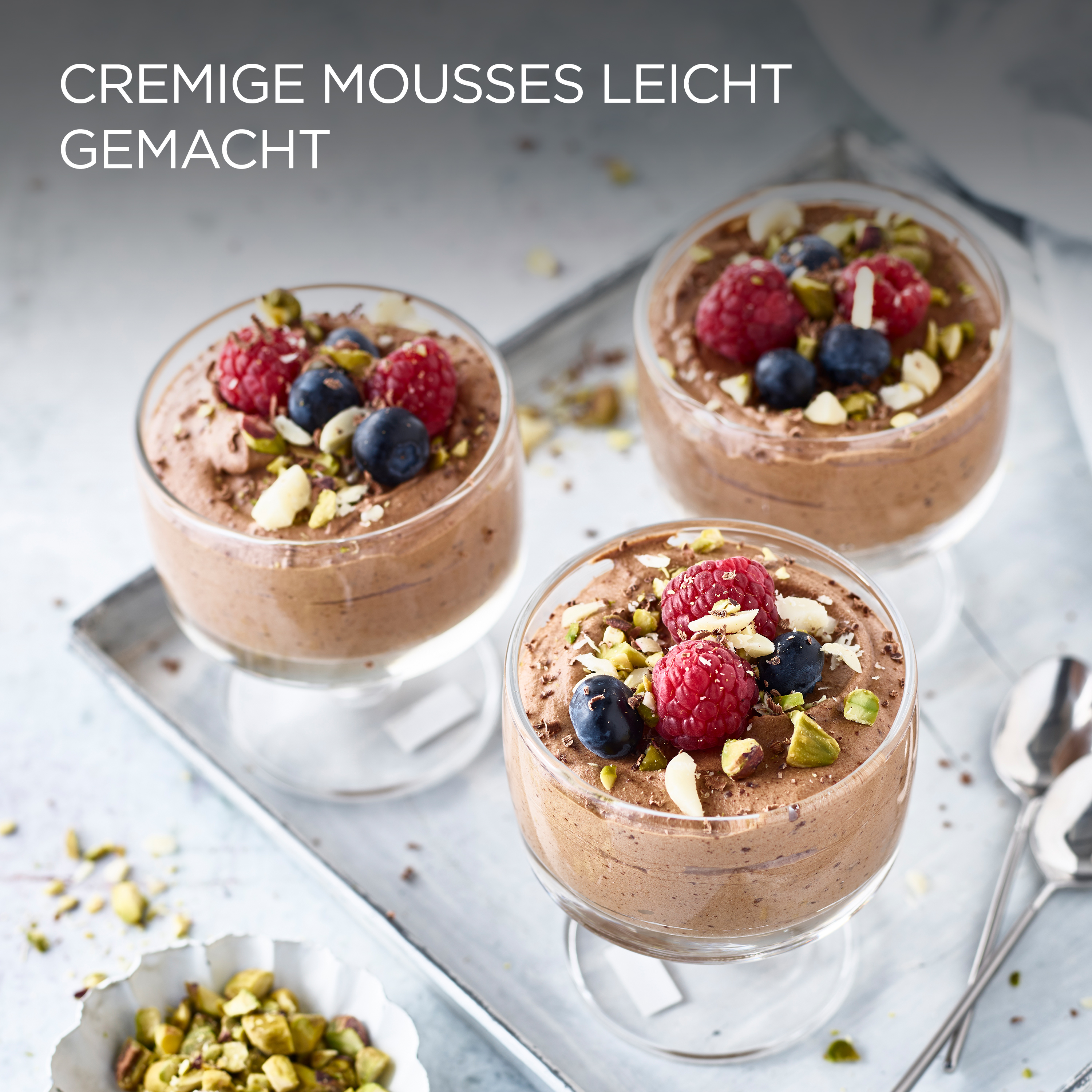 Drei Gläser Schokoladenmousse, belegt mit Beeren und Nüssen, auf einem silbernen Tablett.