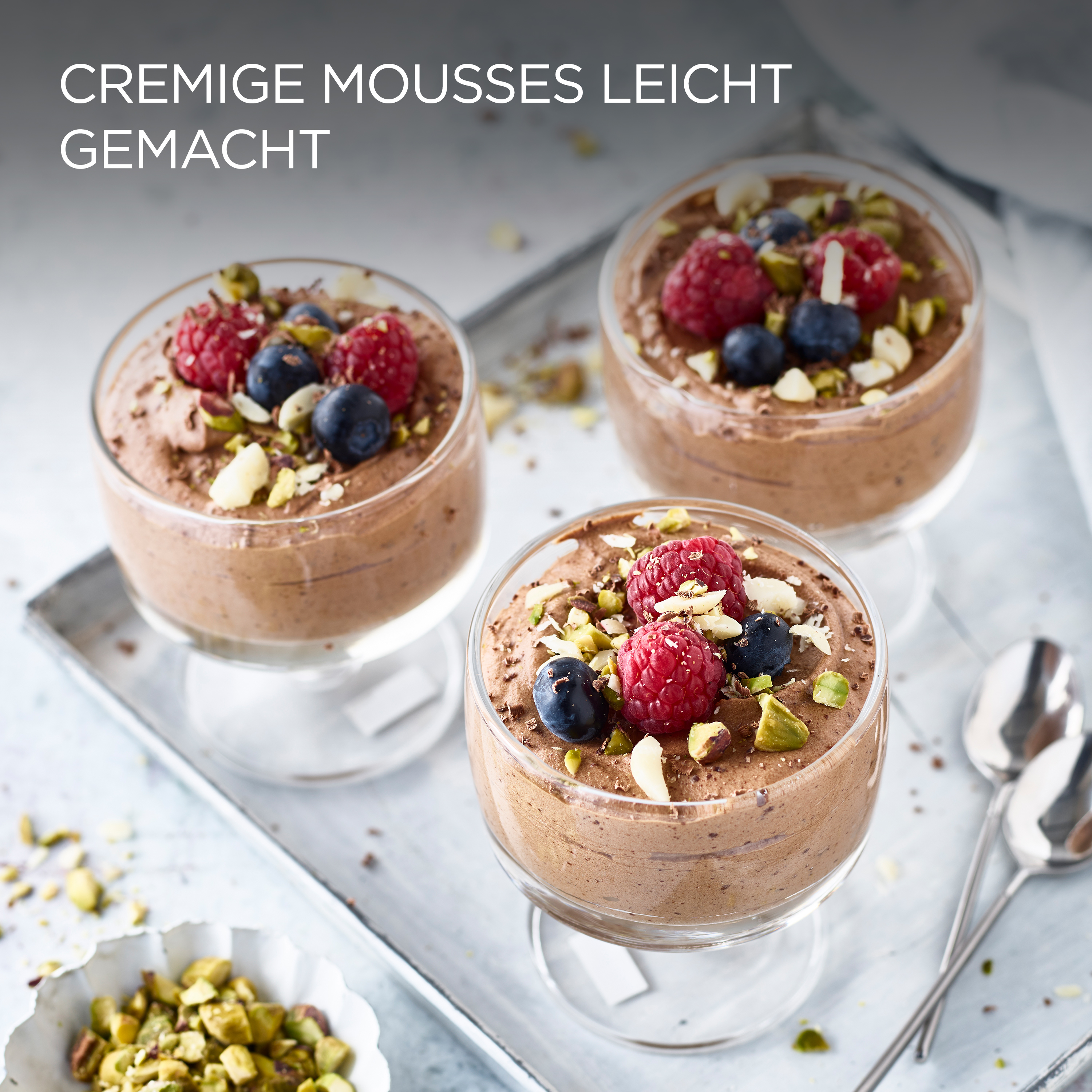 Drei Desserts in Gläsern mit Schokoladenmousse, Beeren und Nüssen auf einem Tablett.