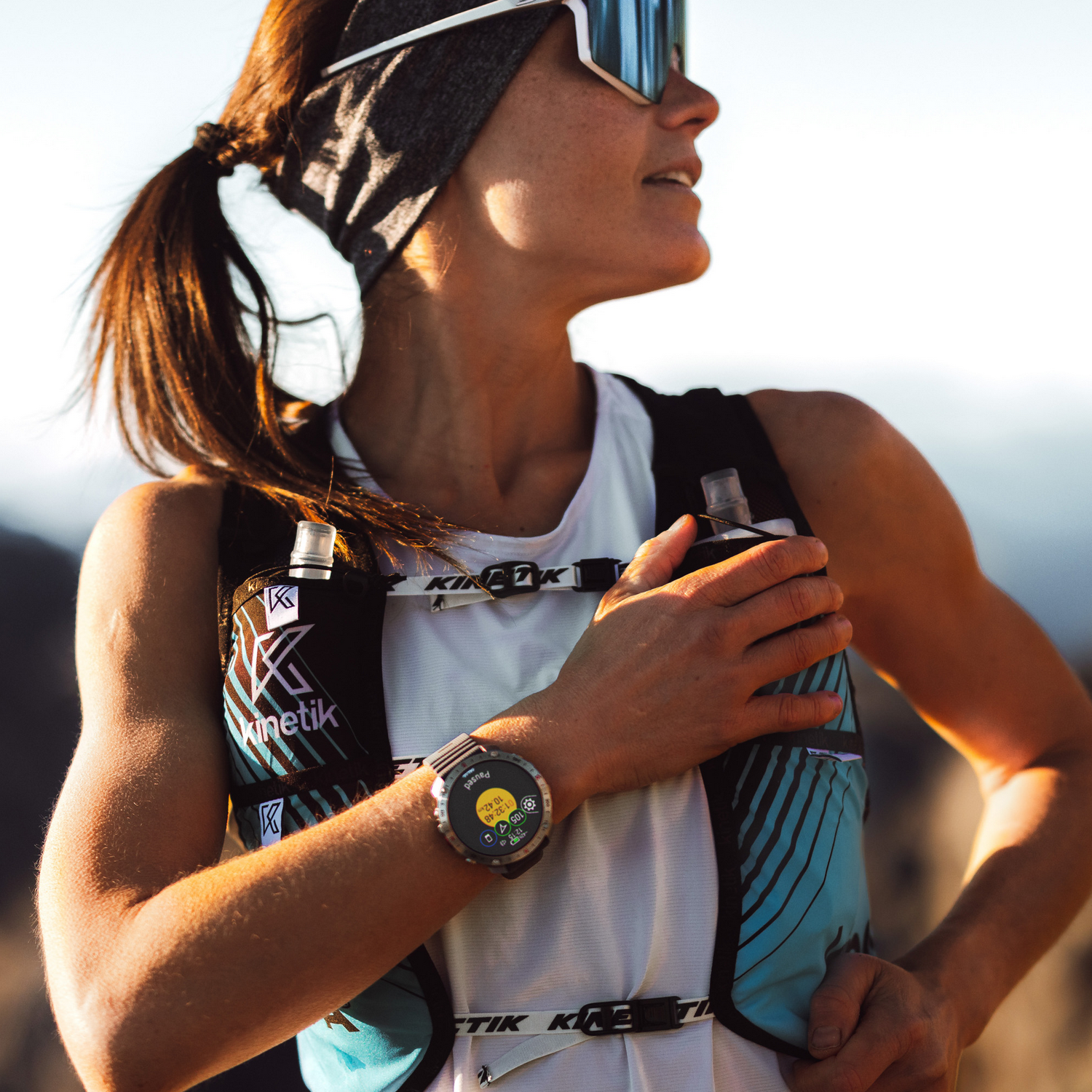 Una mujer con equipo de correr, usando un smartwatch, mirando a lo lejos.