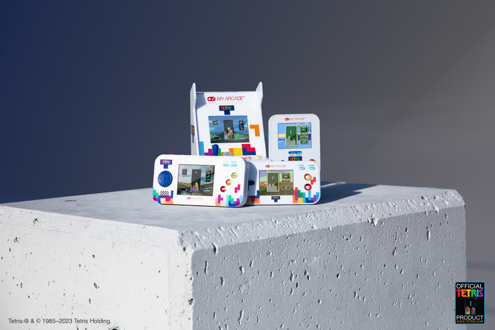 Beton yüzeyde üç el tipi oyun konsolu. Konsolların oyun ekranları ve Tetris markası var.