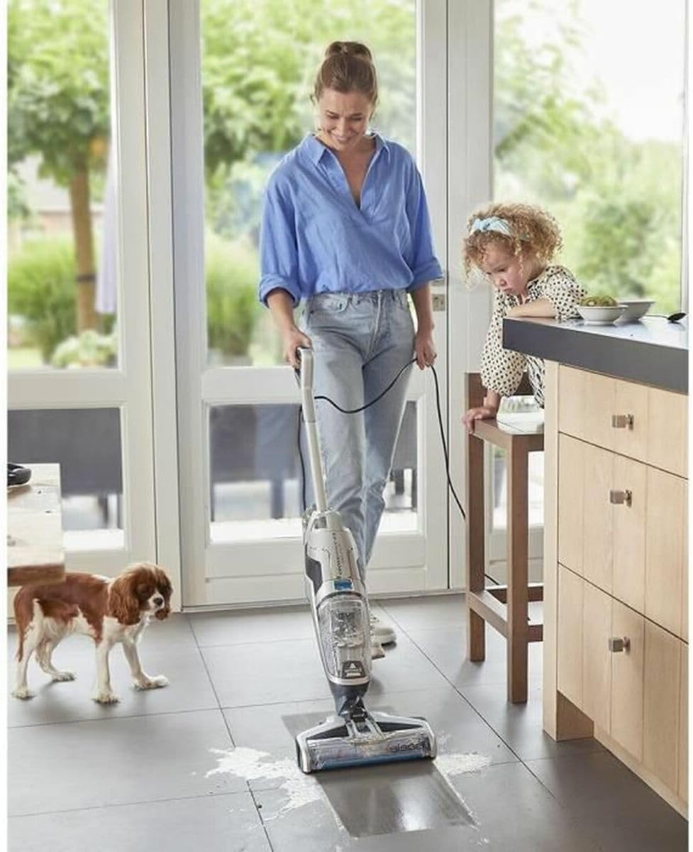Kobieta odkurza szarą podłogę. Pies i dziecko są w pokoju.