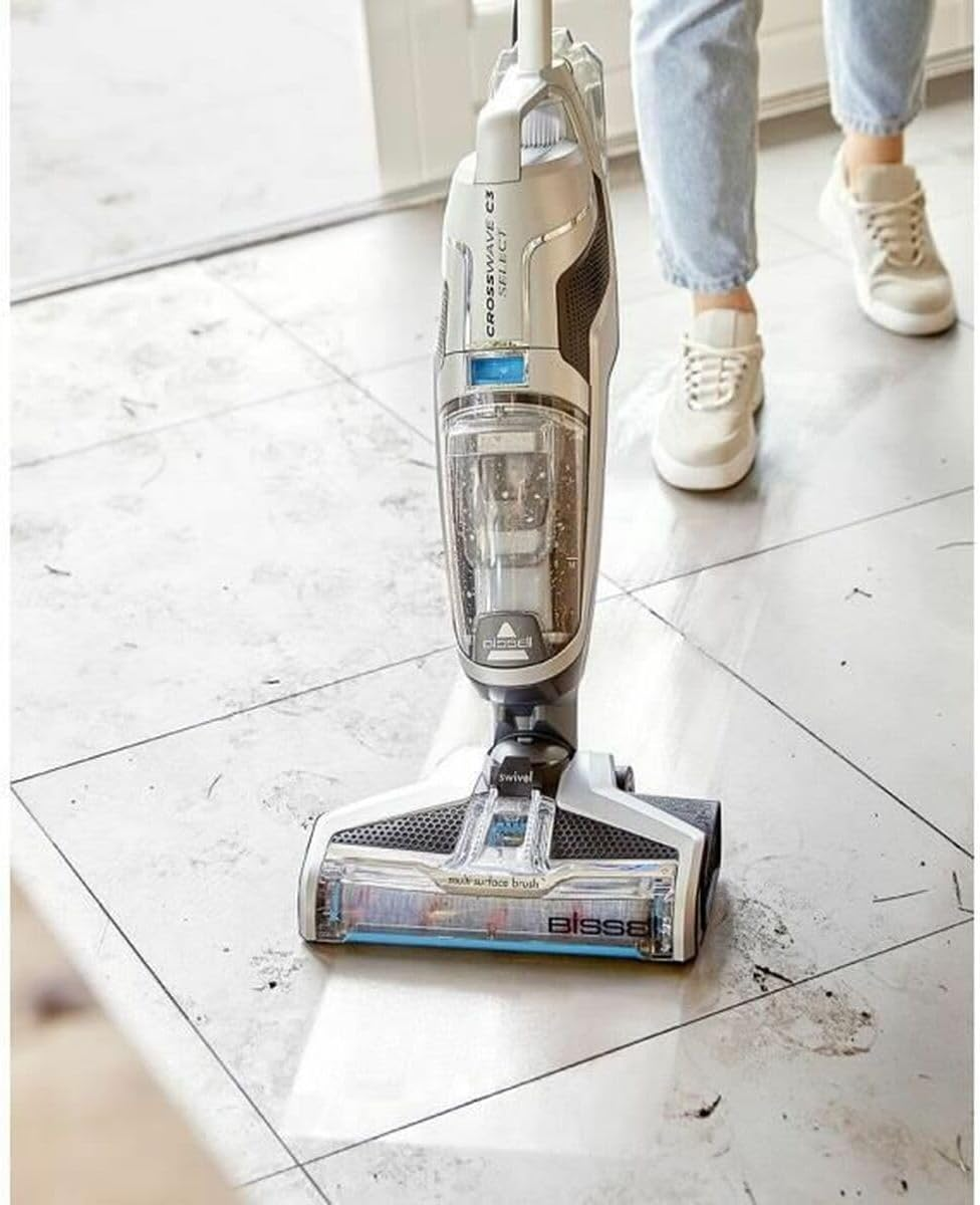 Biały i srebrny odkurzacz czyszczący białą podłogę z płytek, z widocznymi nogami.