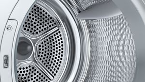 Nahaufnahme eines silbernen Waschmaschinentrommel-Innenraums. Perforiertes Metall, geometrisches Muster und gebogene Metallteile sind sichtbar.