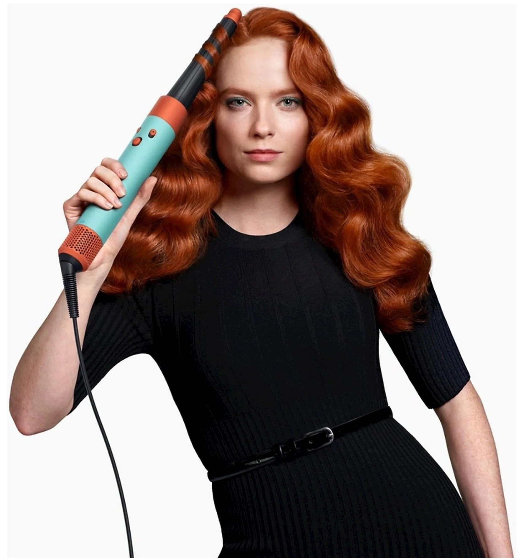 Kobieta z rudymi włosami trzyma lokówkę. Czarna sukienka i tło.