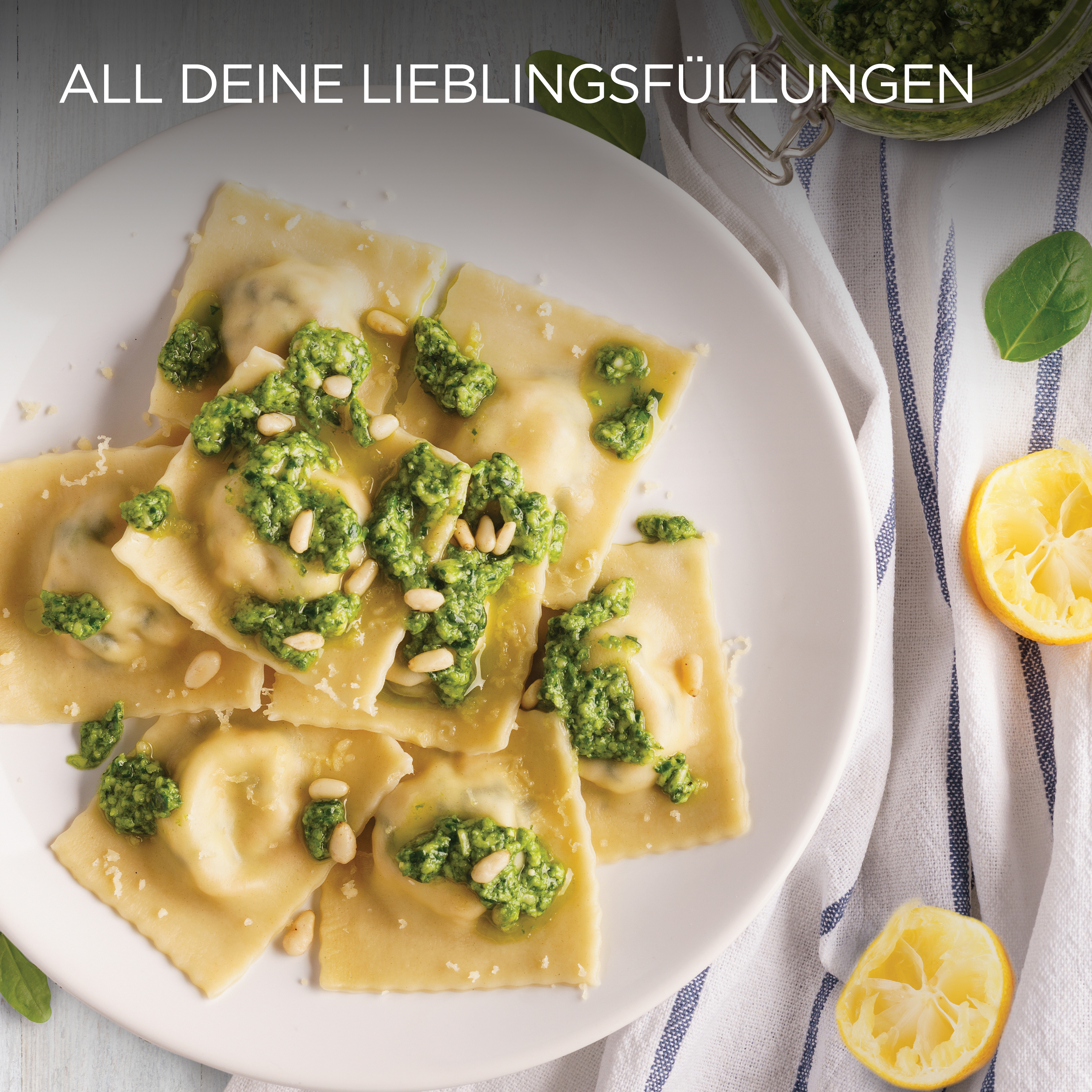 Teller Ravioli mit Pesto, Pinienkernen und Zitronenscheiben auf weißer Oberfläche.