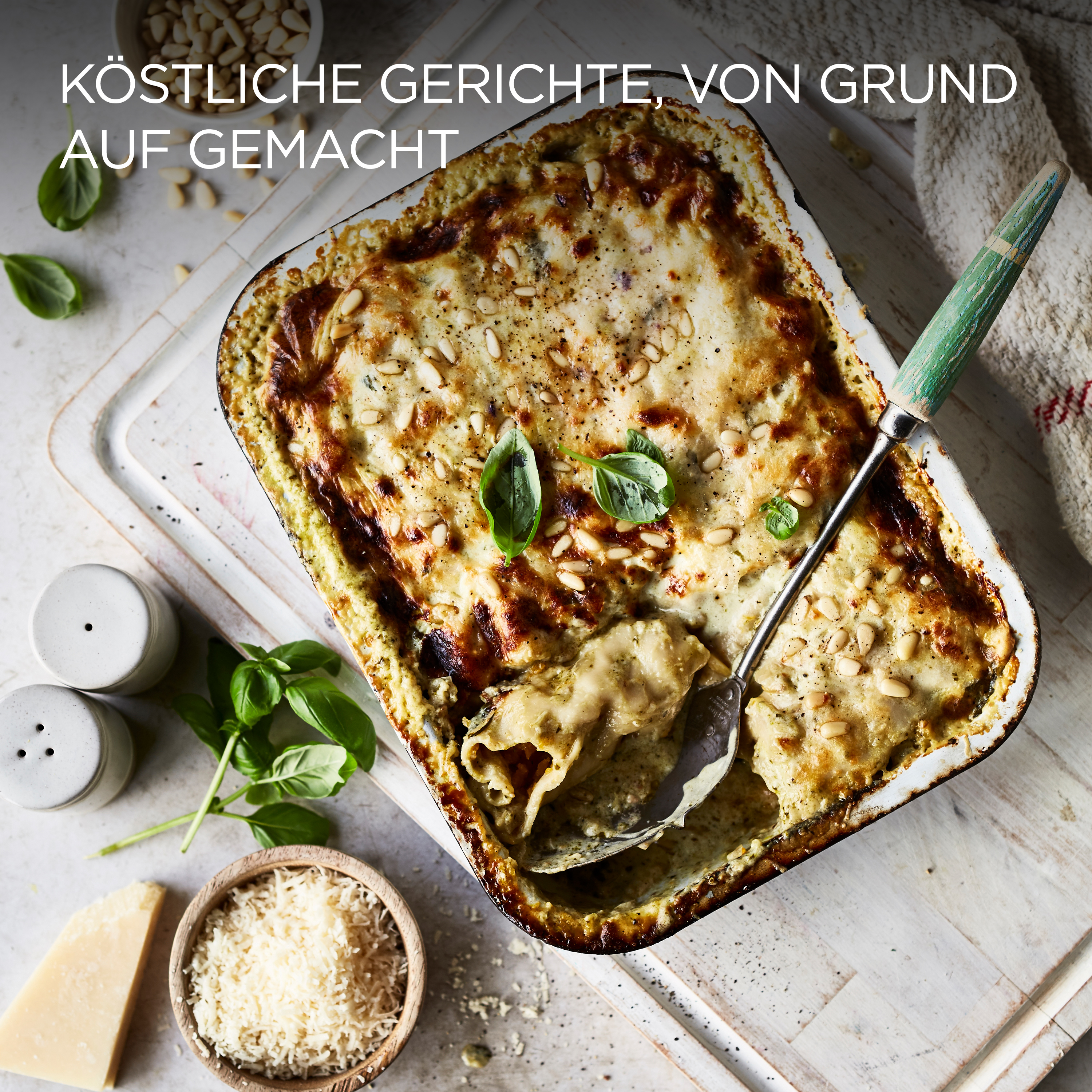Lasagne in weißer Schale, mit Basilikum und Pinienkernen.