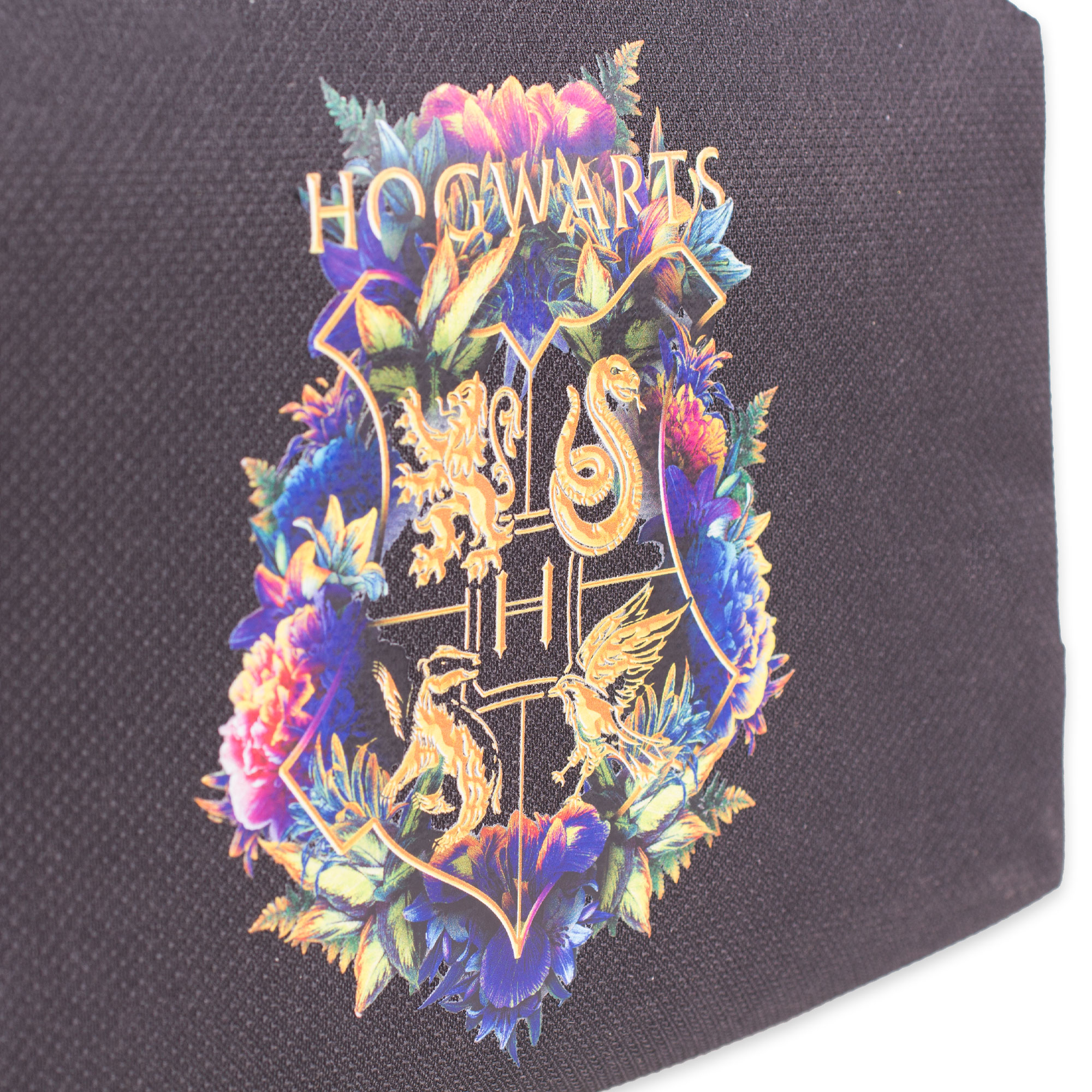Nahaufnahme eines floralen Hogwarts-Wappens auf schwarzer Stoffoberfläche.