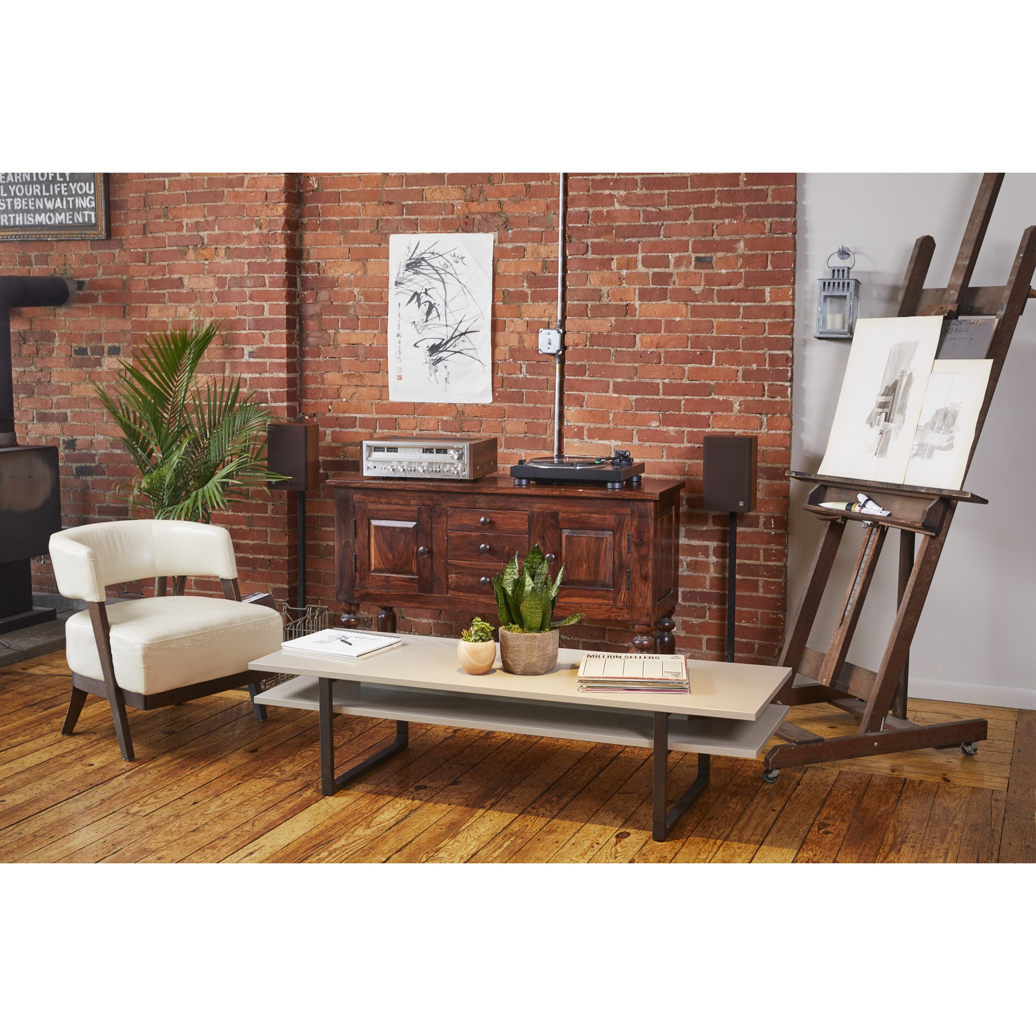 Un soggiorno con divano, tavolo, dipinti e pavimento in legno. Una pianta è sul tavolo.