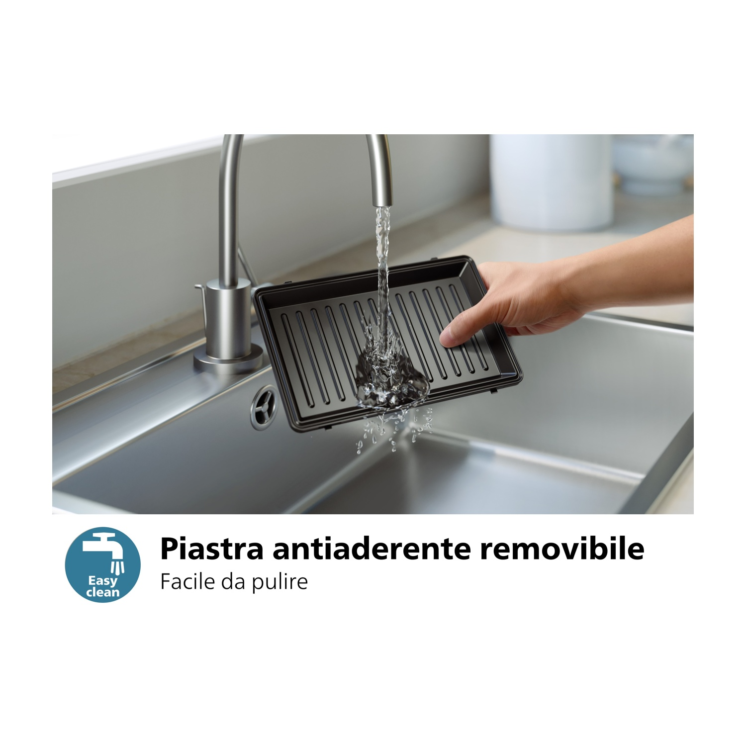 Mano che lava una bistecchiera nera in un lavello in acciaio inox sotto un rubinetto. Testo facile da pulire.