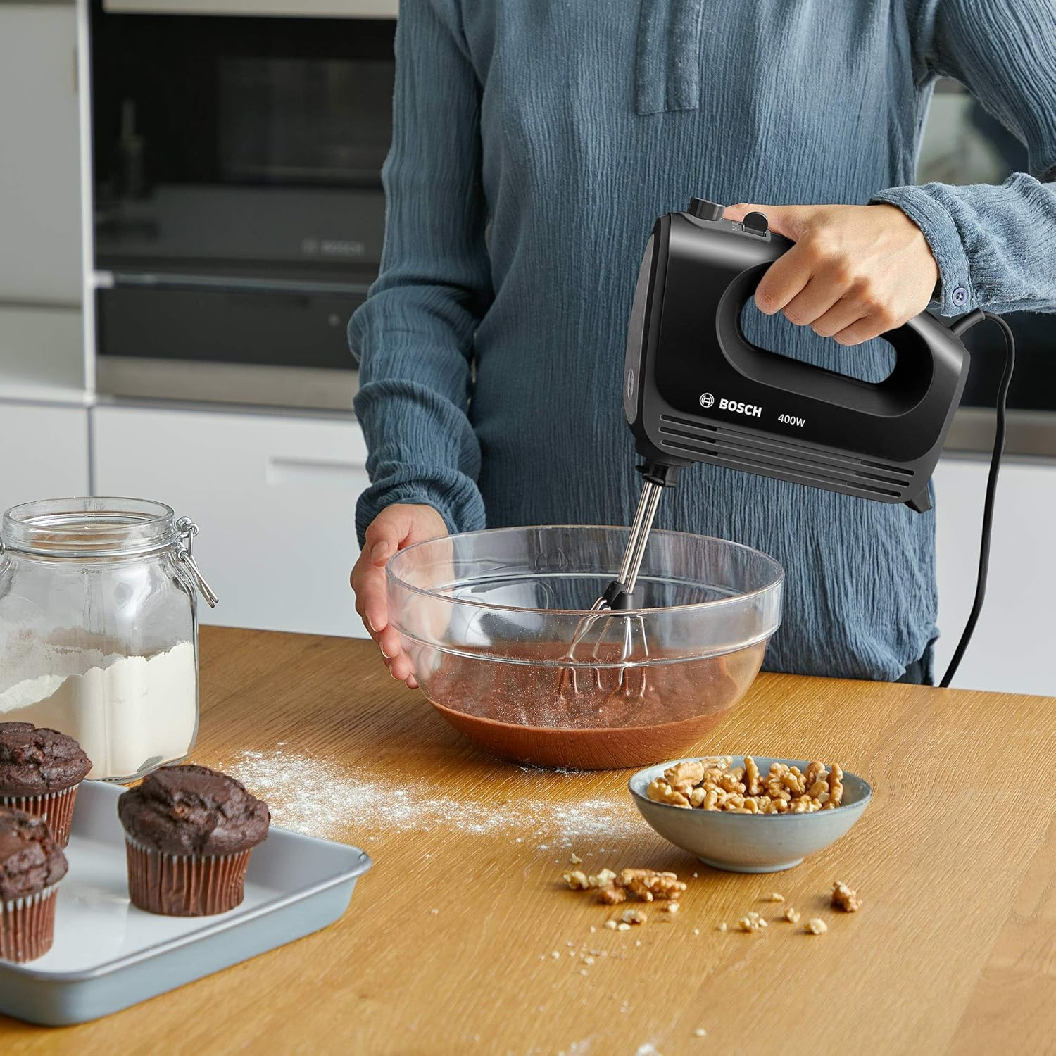 Osoba używa czarnego miksera ręcznego Bosch do mieszania składników w szklanej misce. Kuchnia.