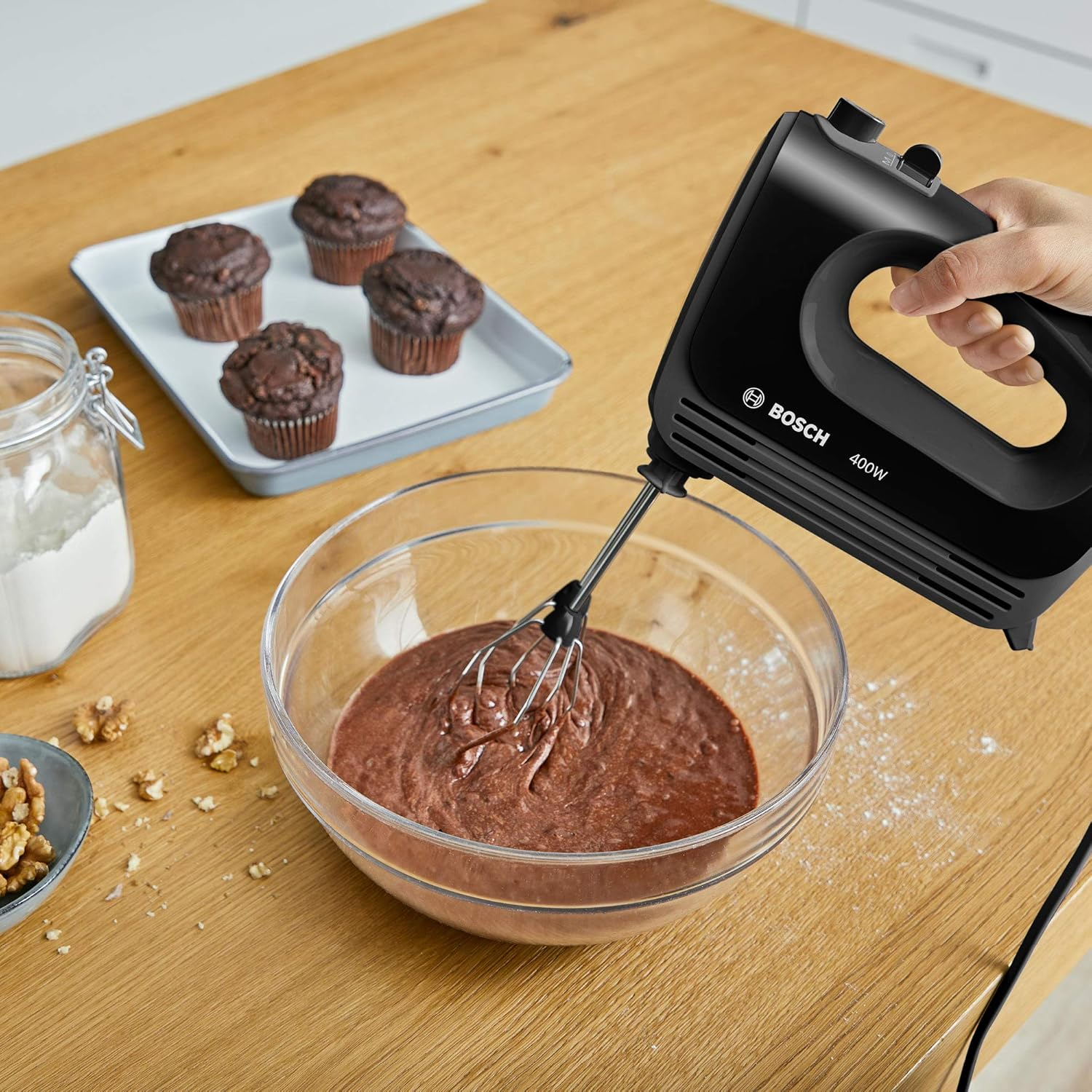 Mikser ręczny mieszający ciasto w misce. Babeczki na tacy na stole.