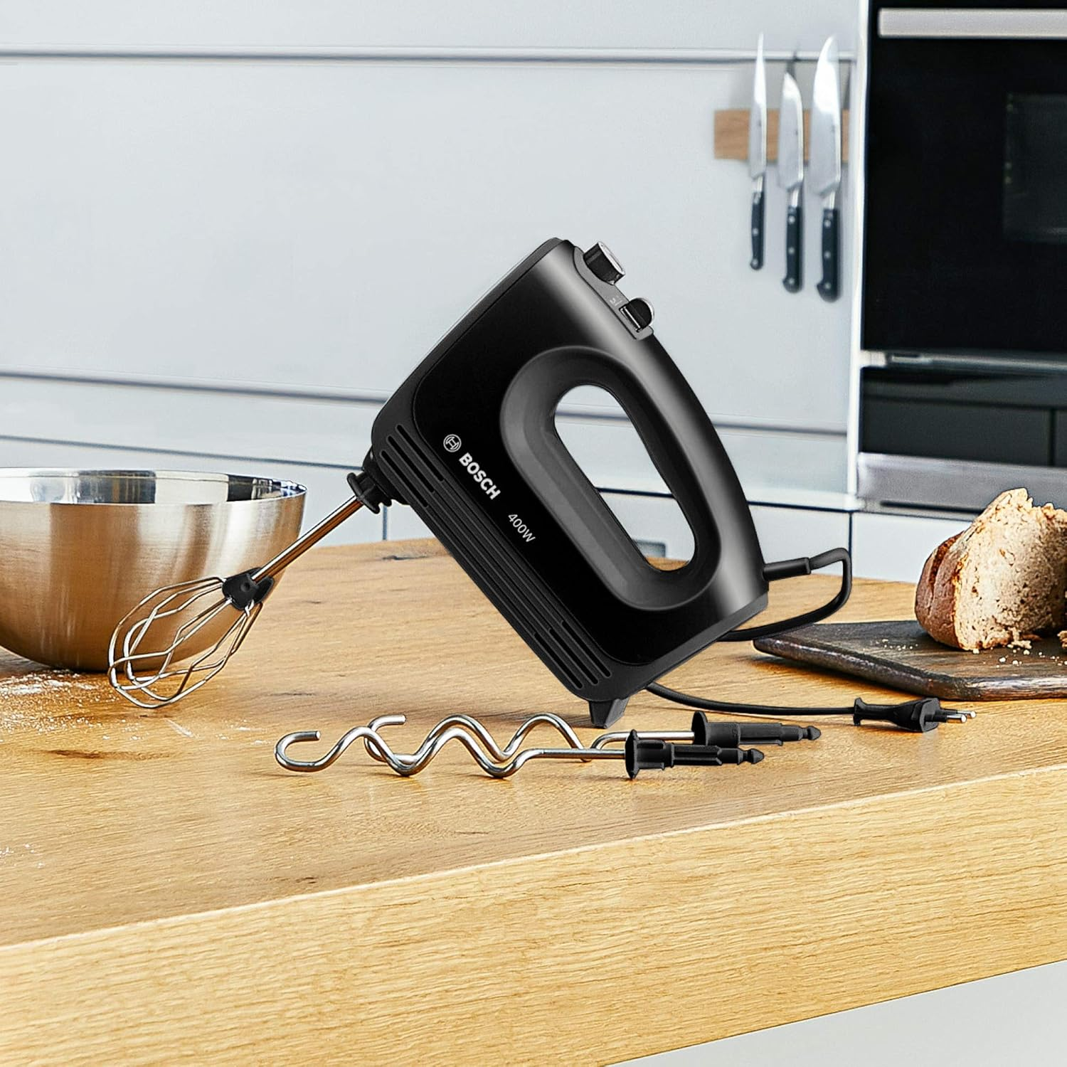 Czarny mikser ręczny z trzepaczką i końcówkami na drewnianej powierzchni. Widoczne noże i miska.