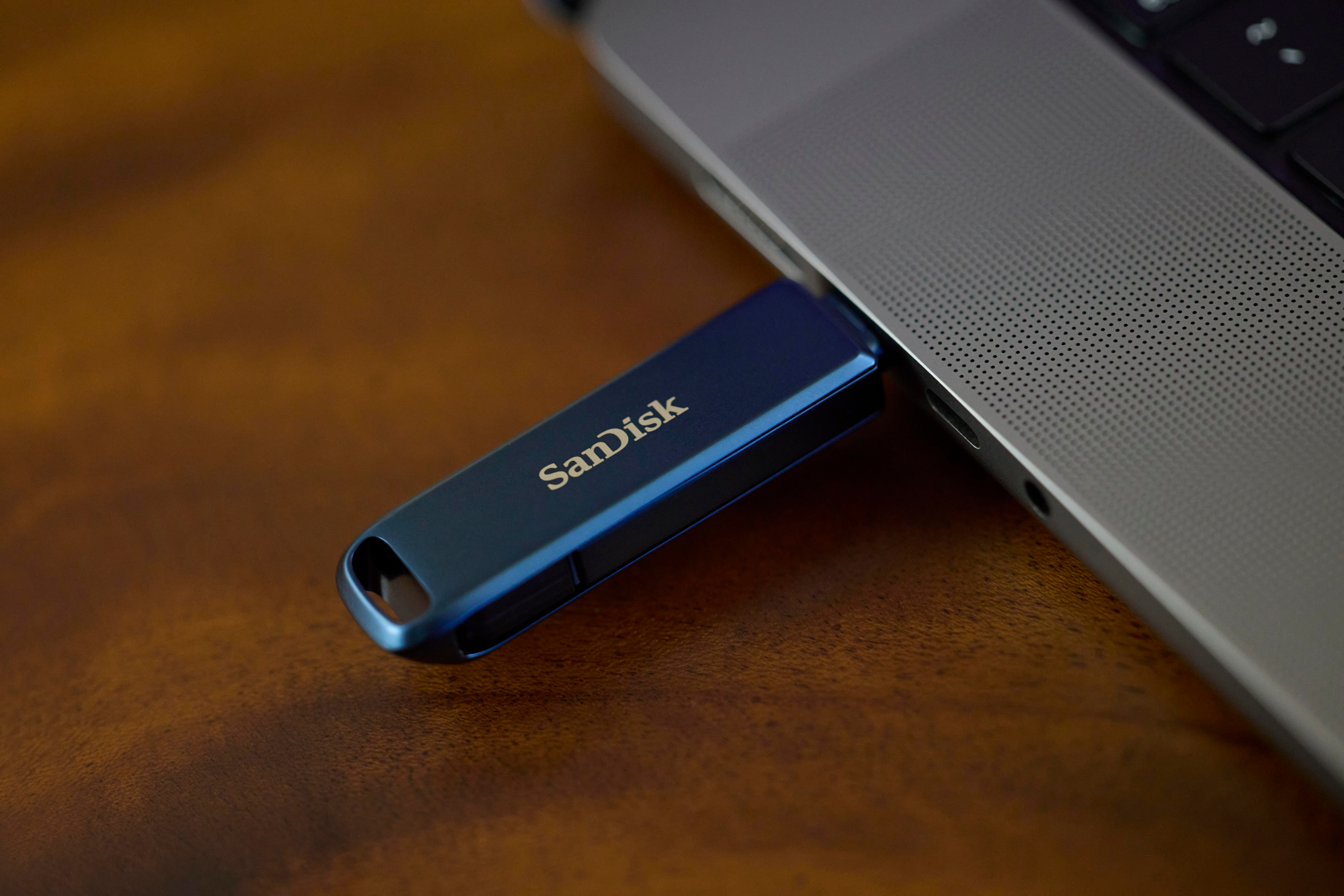 Ein blauer USB-Stick wird in einen Laptop auf einem Holztisch gesteckt.