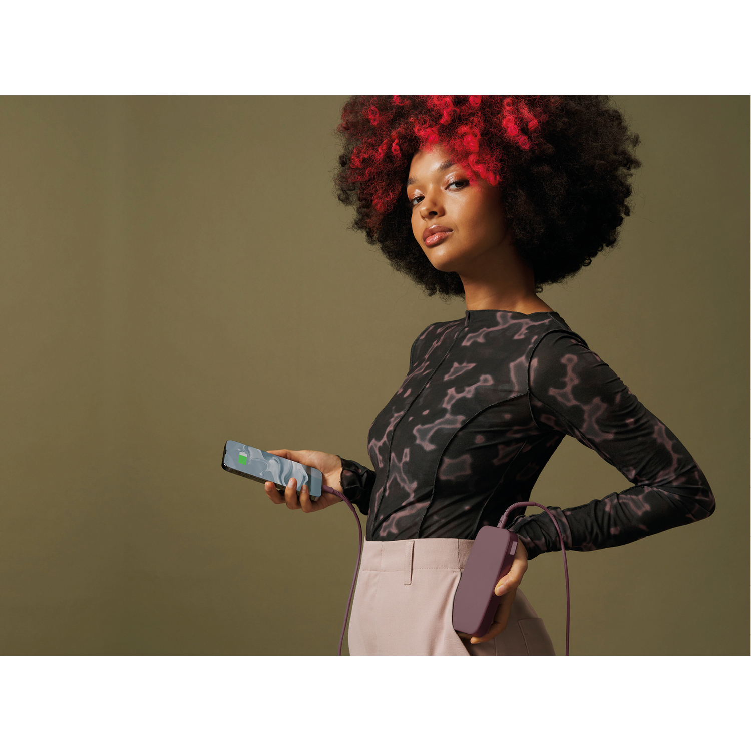 Femme chargeant un téléphone avec une batterie externe violette. Fond vert et cheveux rouges.