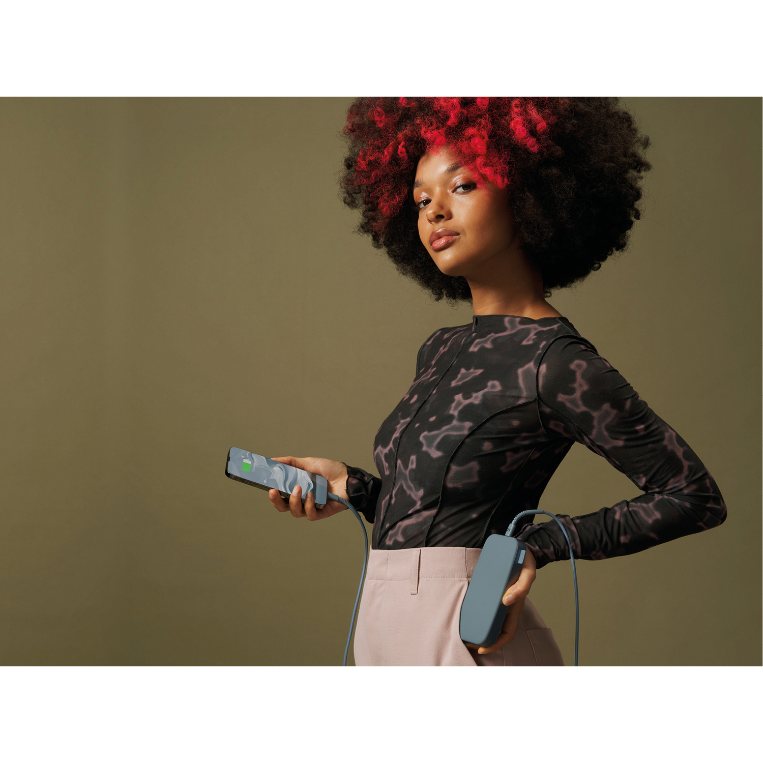 Femme tenant un téléphone et une batterie externe. Le téléphone affiche 75% de charge.